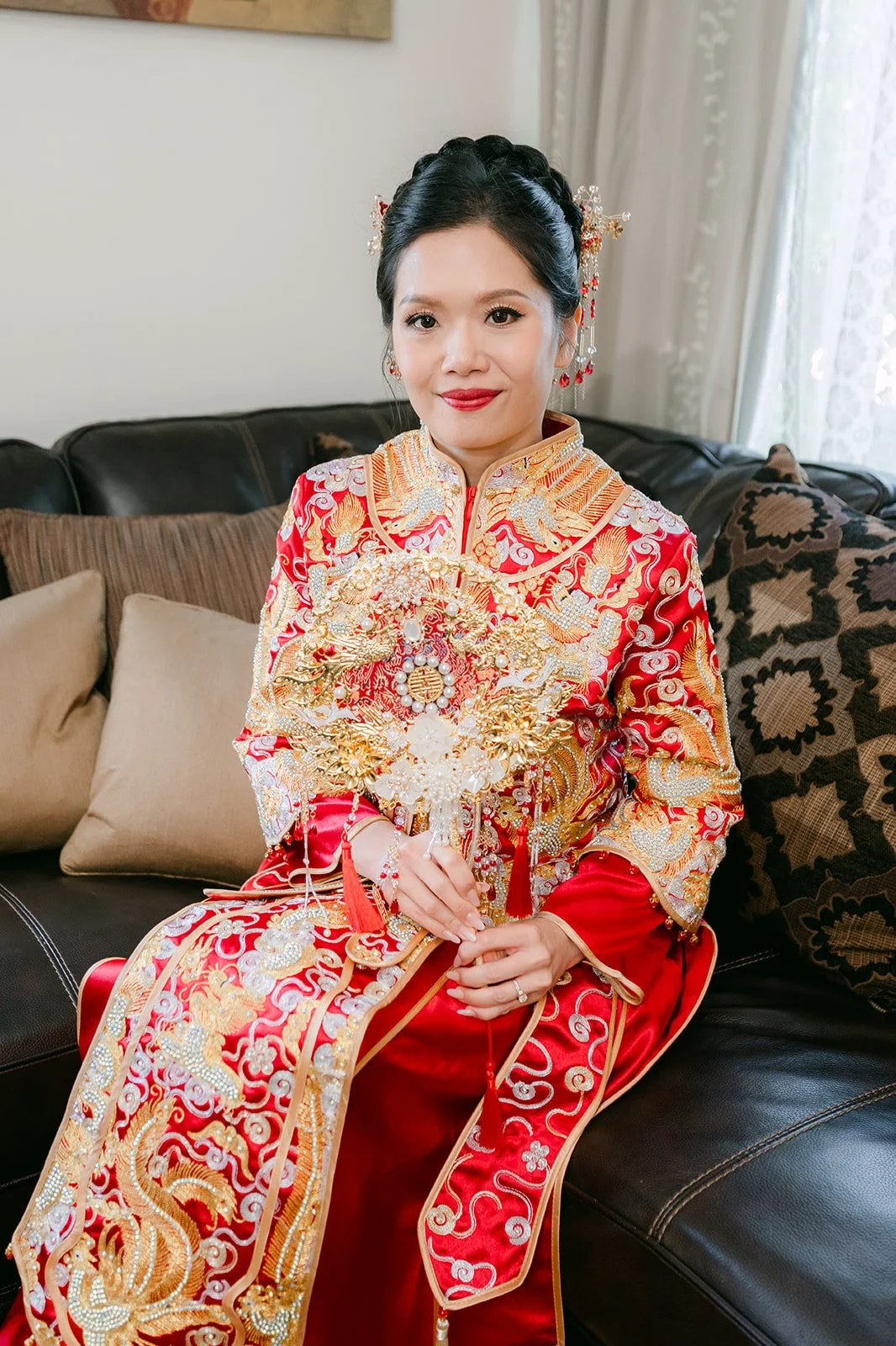 A bride in a gold and red qun kwa sitting on a leather sofa.