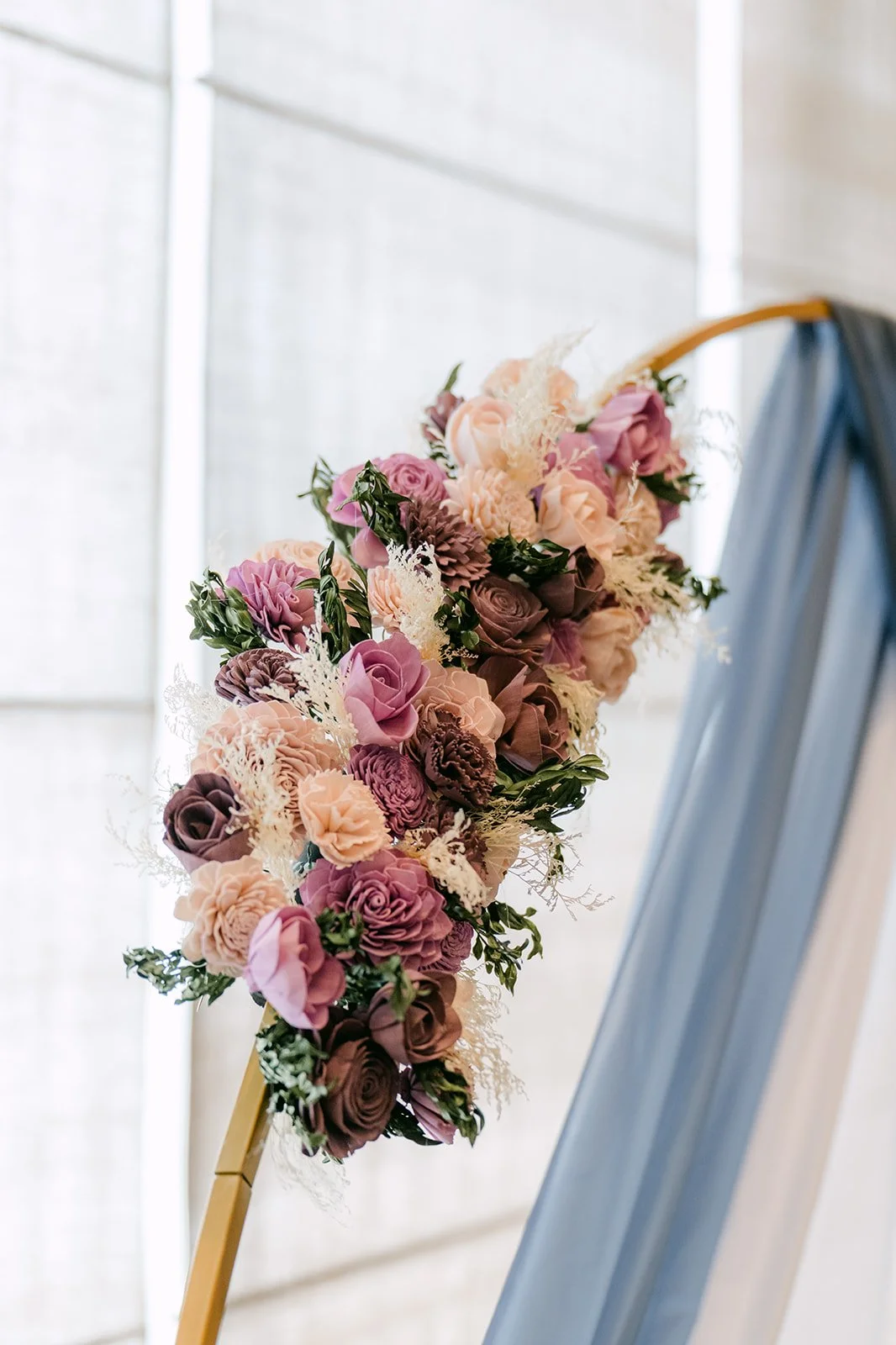 Lavender and mauve florals on the gold arch with dusty blue draping.