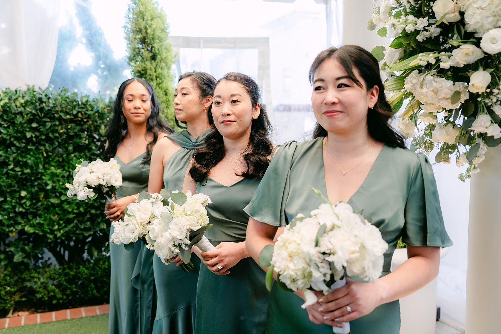 Bridesmaids in sage green holding white bouquets during the ceremony