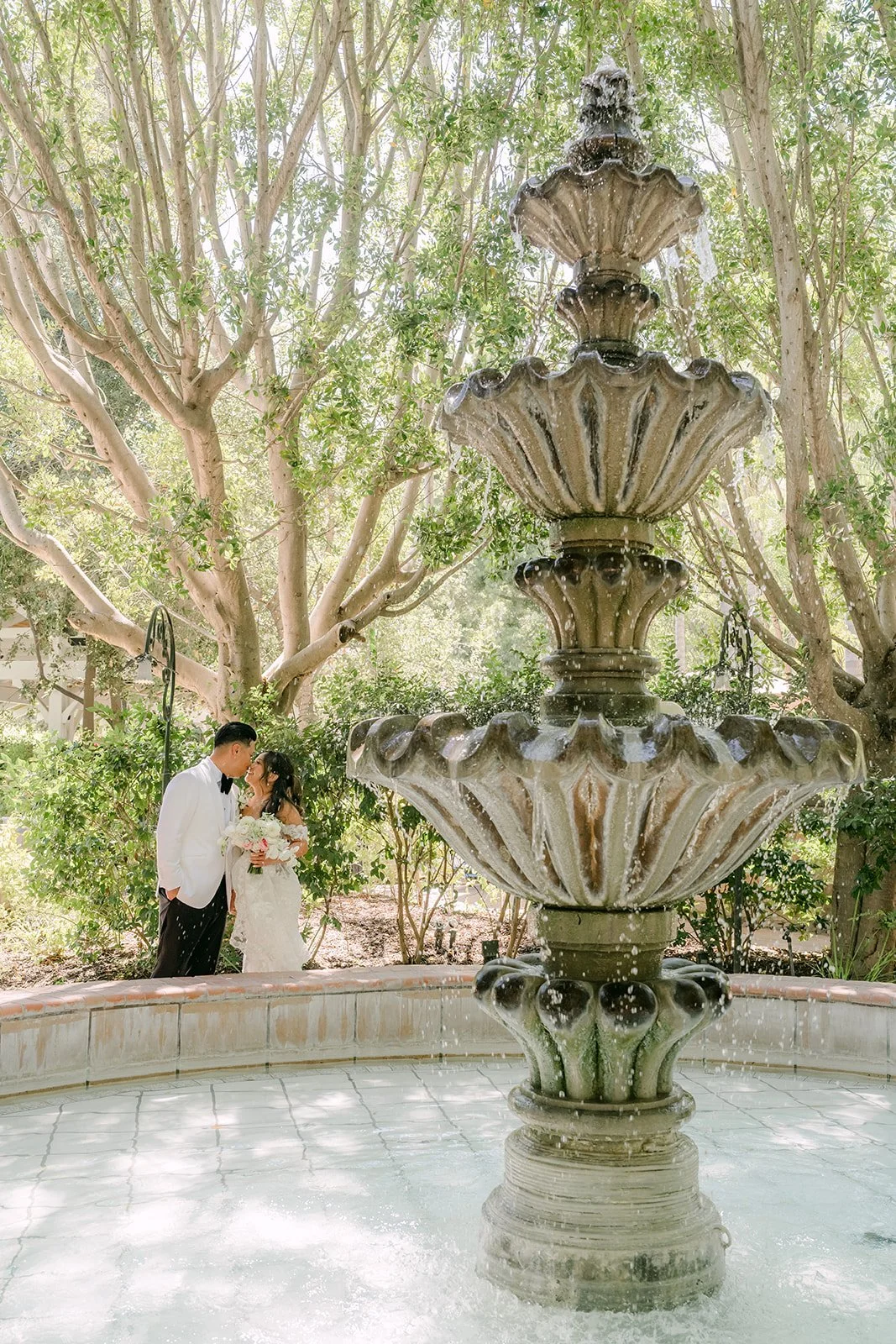 Nicole and Caryl kissing beside the tiered fountain at Eden Gardens.