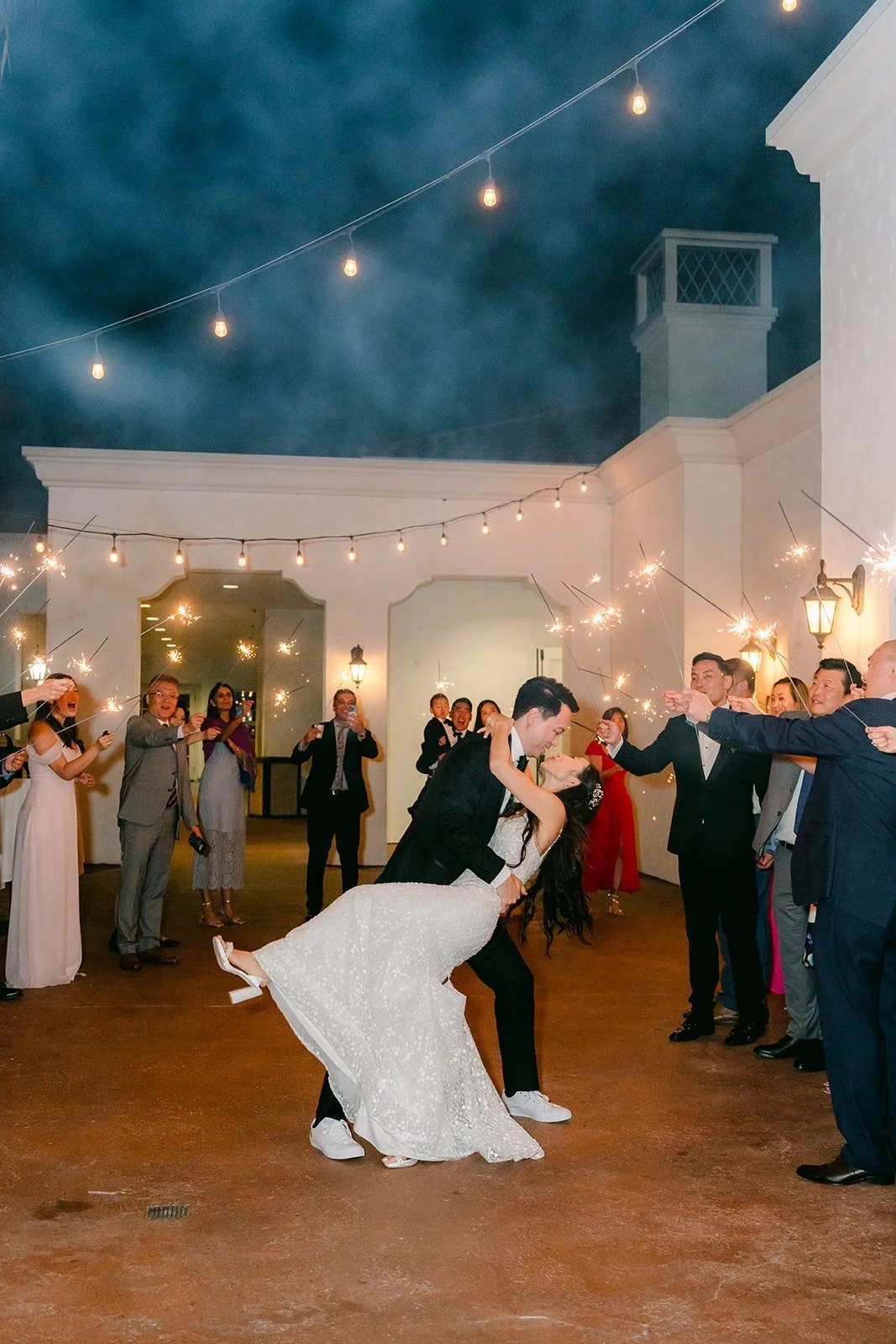 William dipping Kristine for a kiss under the string lights during the sparkler send off