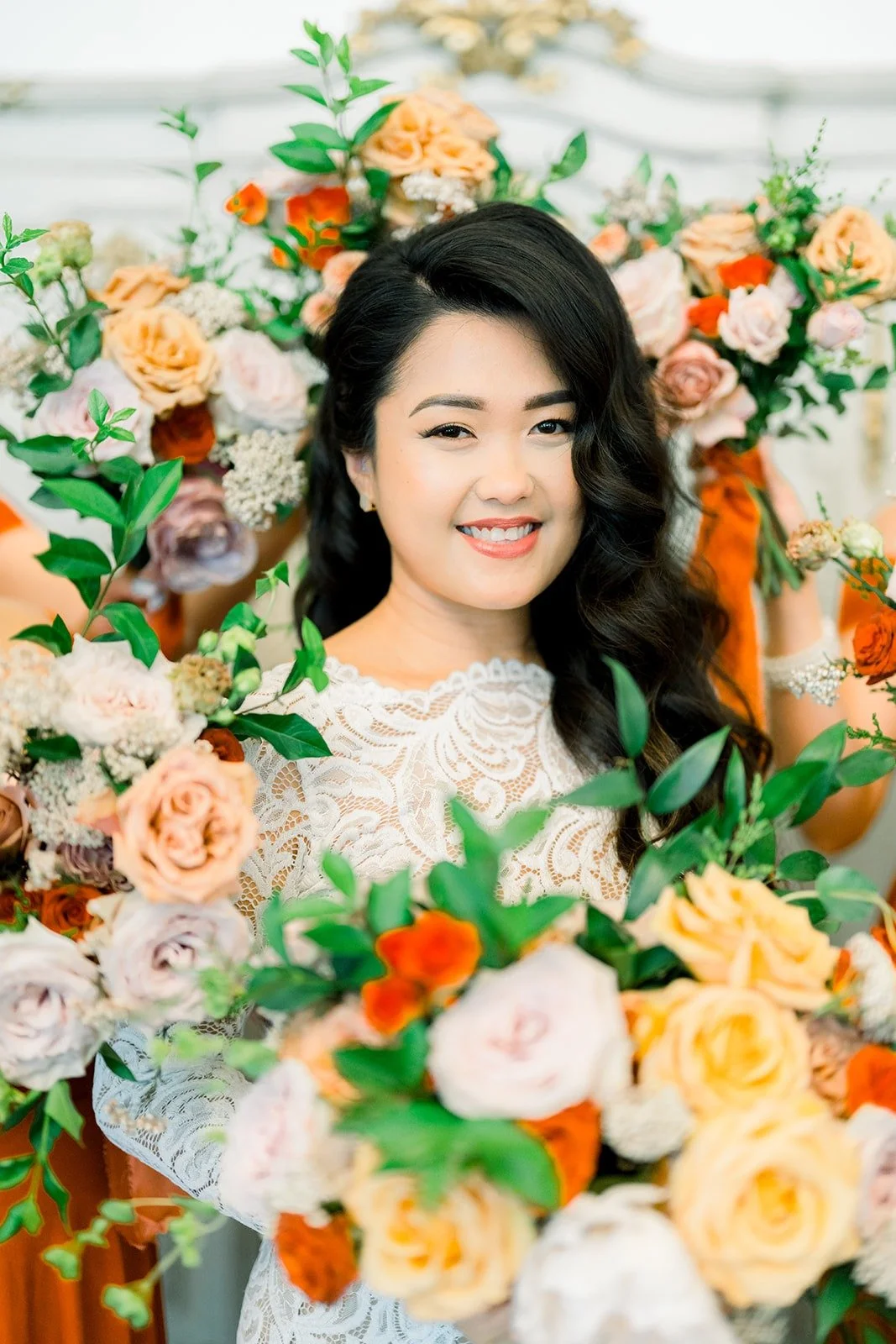 Hannah smiling behind her bouquet of peach, blush and orange roses
