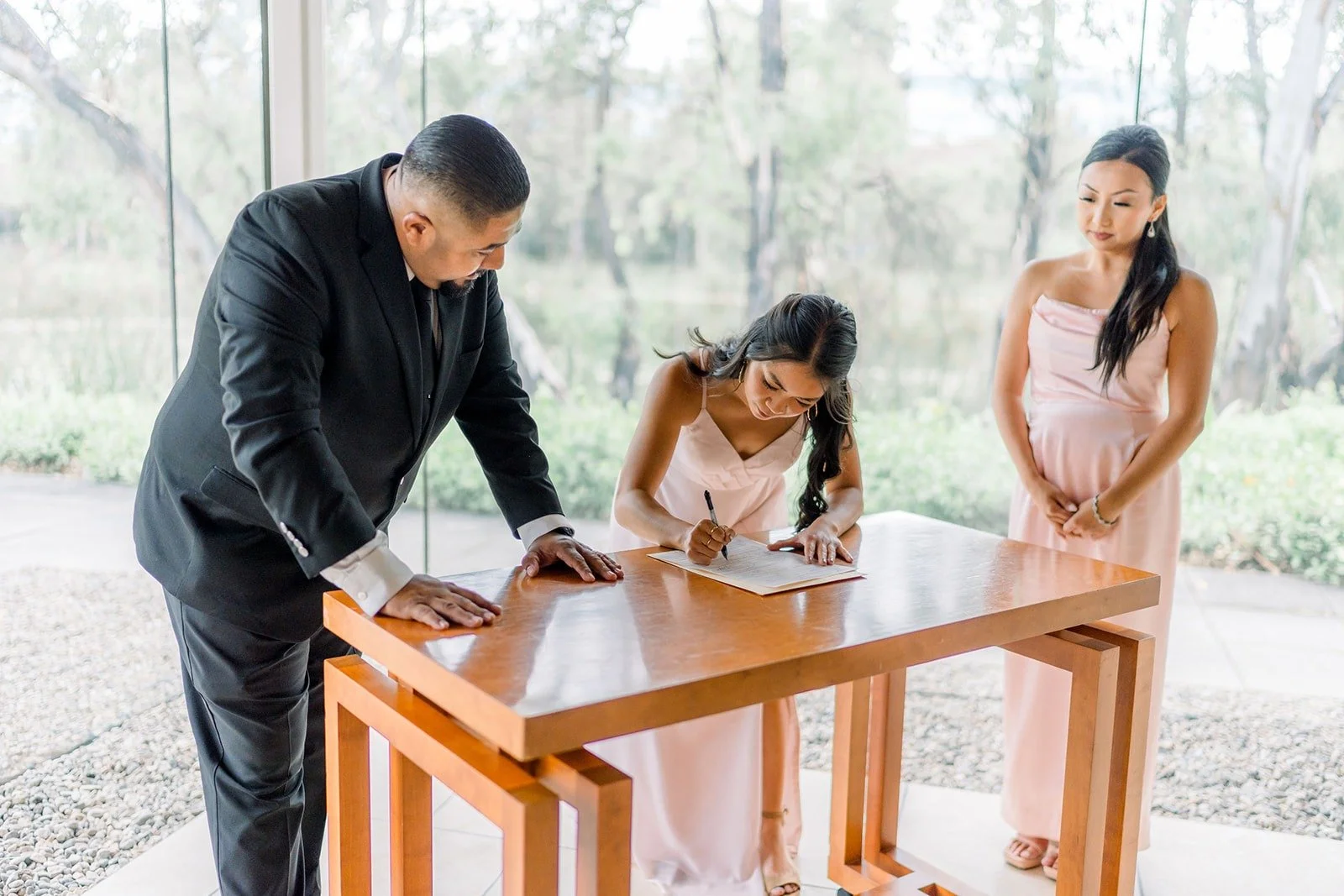 Steven and Jacinda sign at a wooden table, photographed by One and Only Production