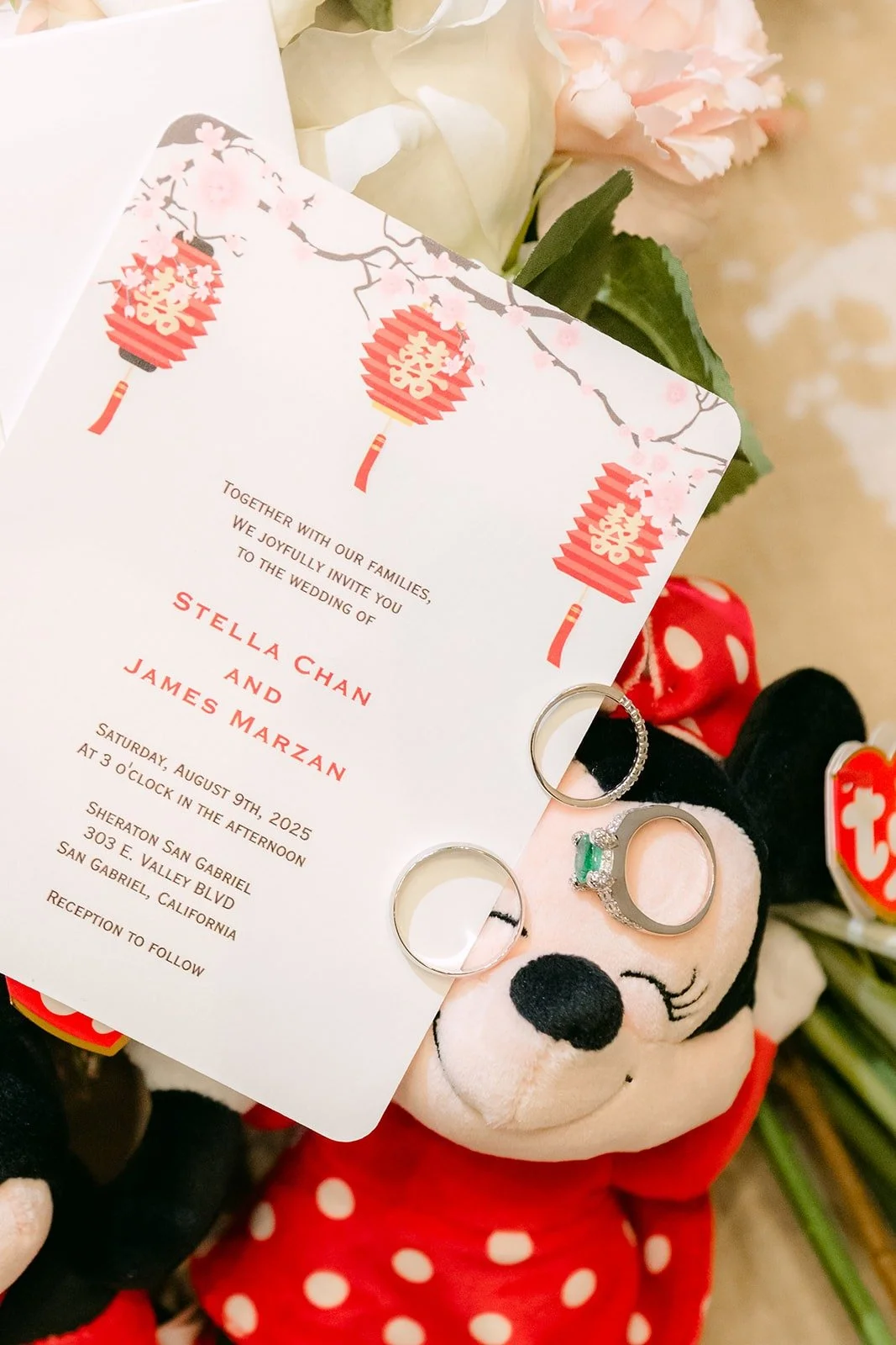 A wedding invitation with red lantern details and the couple's rings resting beside a Minnie plush