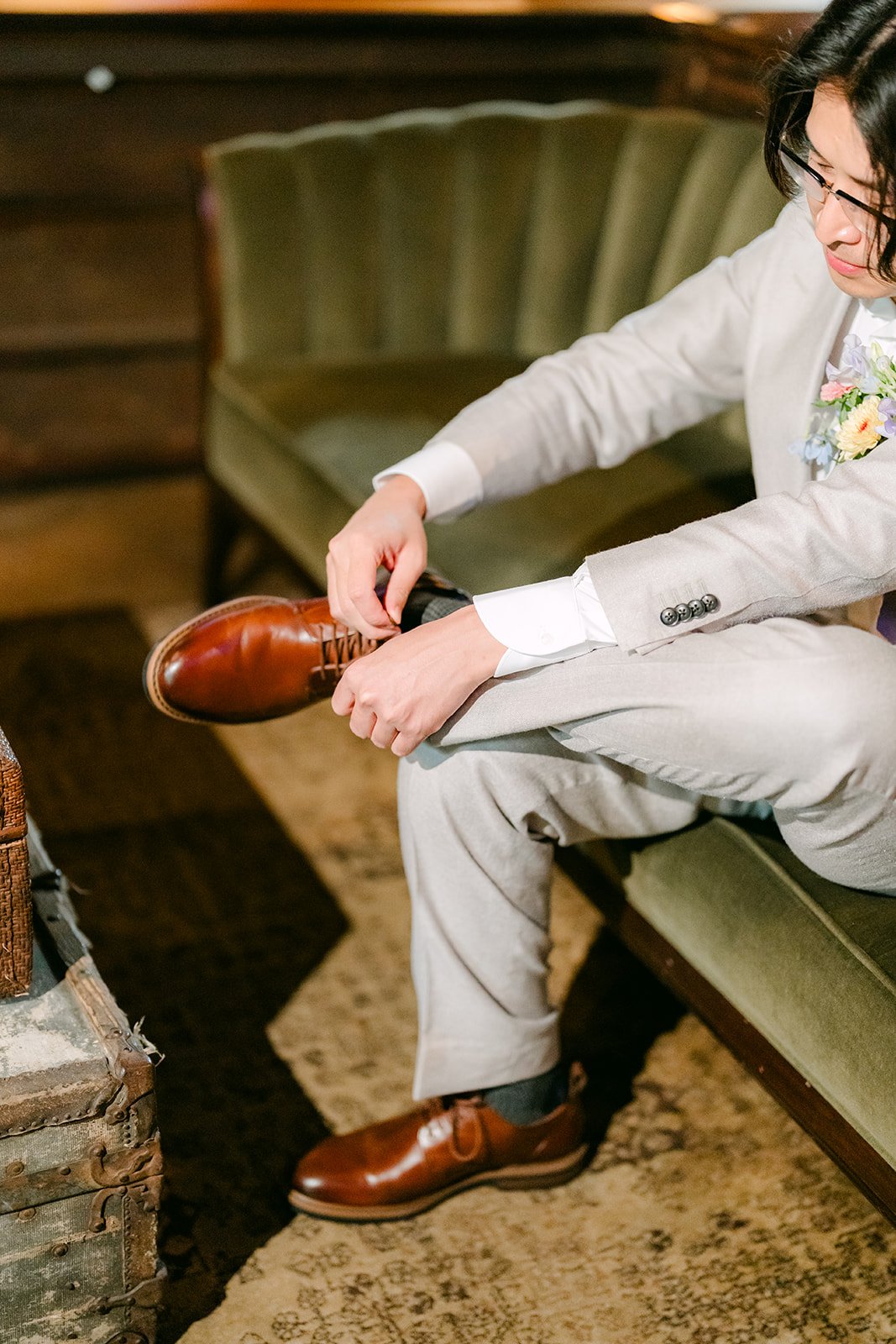 Mike tying his brown dress shoes on a green velvet sofa