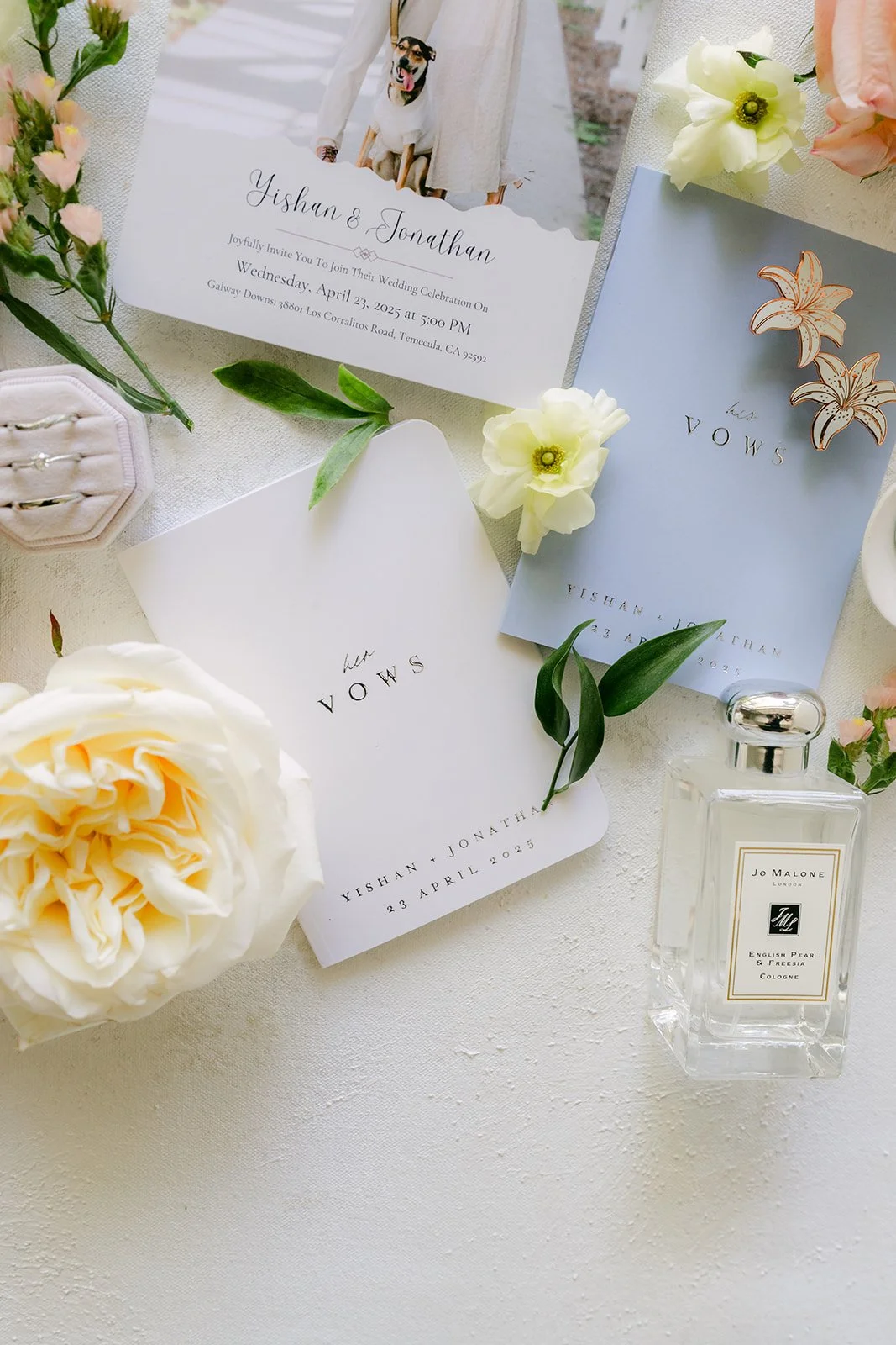 Wedding invitation suite with cream roses and a perfume bottle in a flat lay