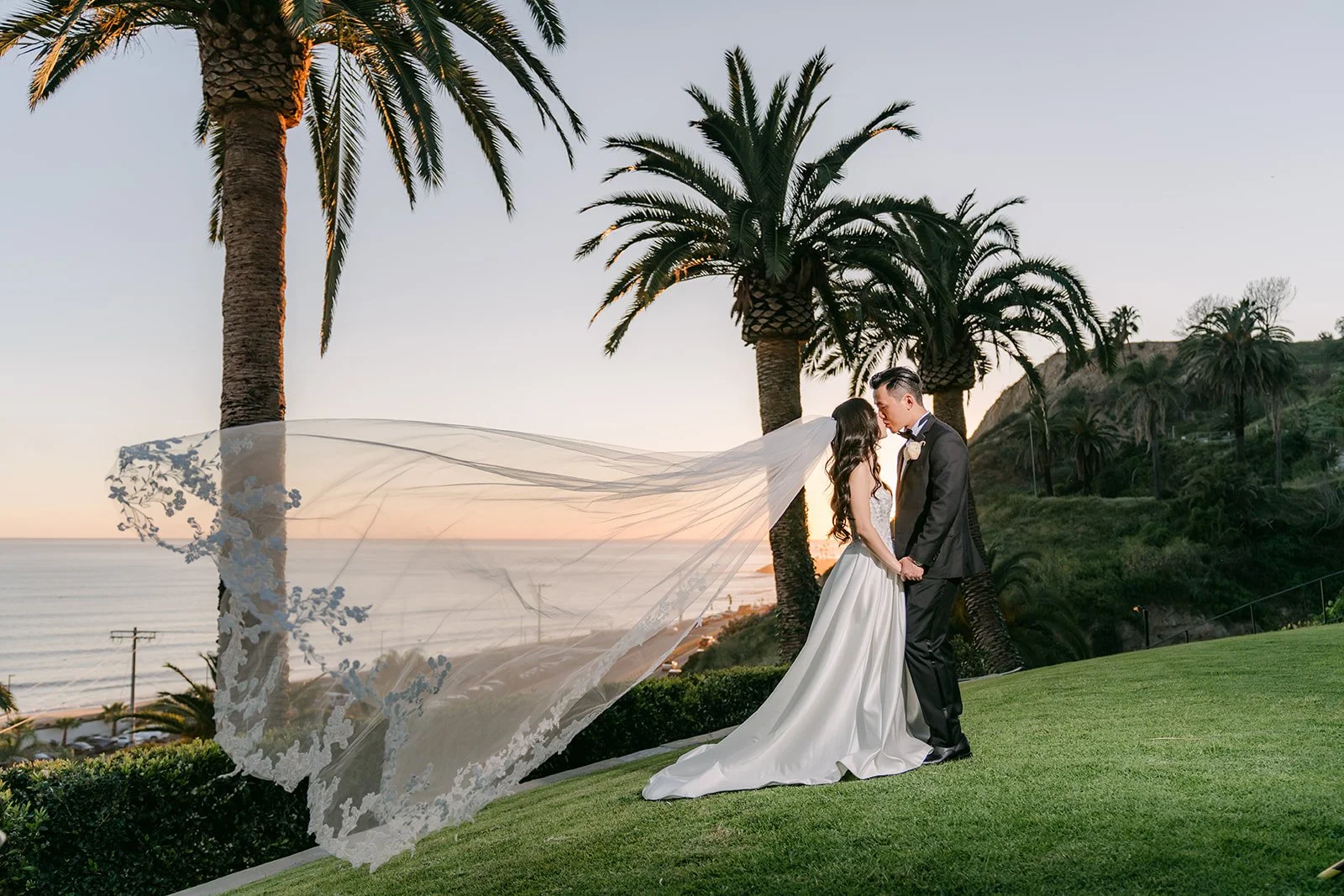 Veil flowing in the wind as the couple kisses at sunset