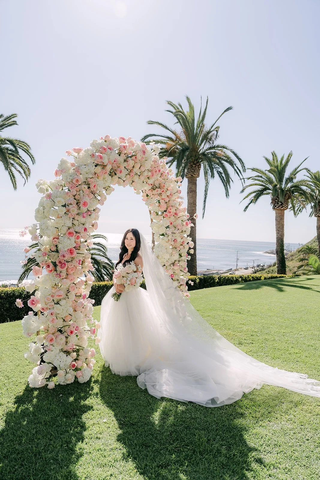 Bride posing with her bridesmaids beside the floral arch