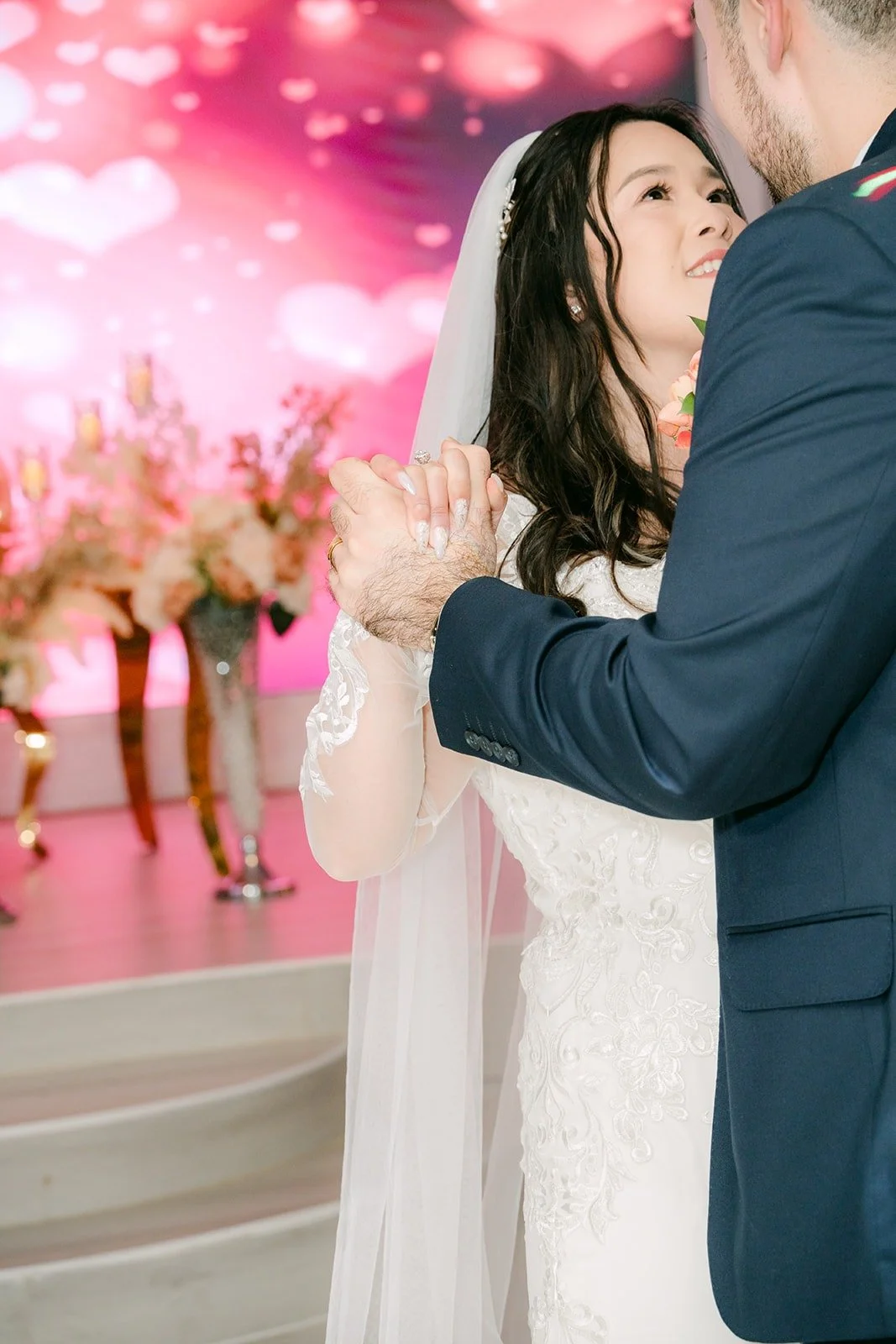 Amy smiling up at James during their first dance against a pink glow