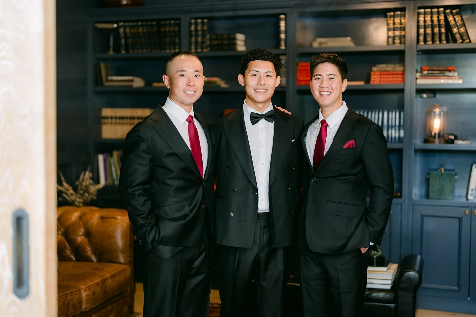 Richard with two groomsmen in front of the navy bookshelves