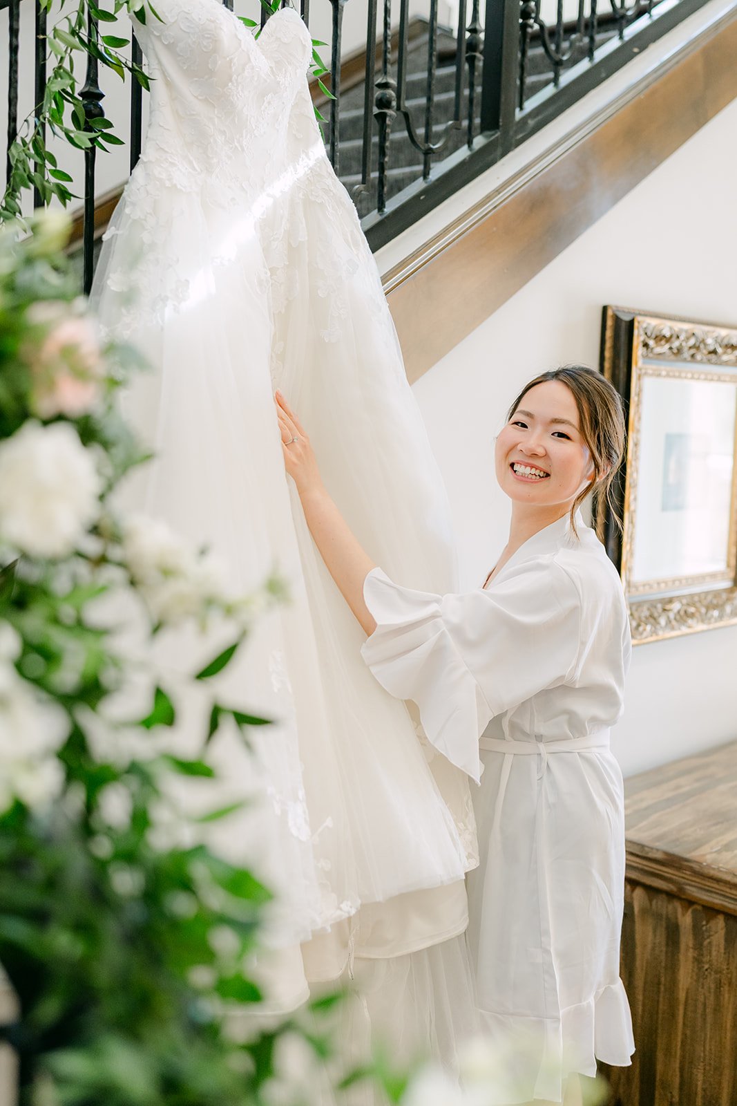 Victoria smiling beside her wedding gown on the garland-wrapped staircase