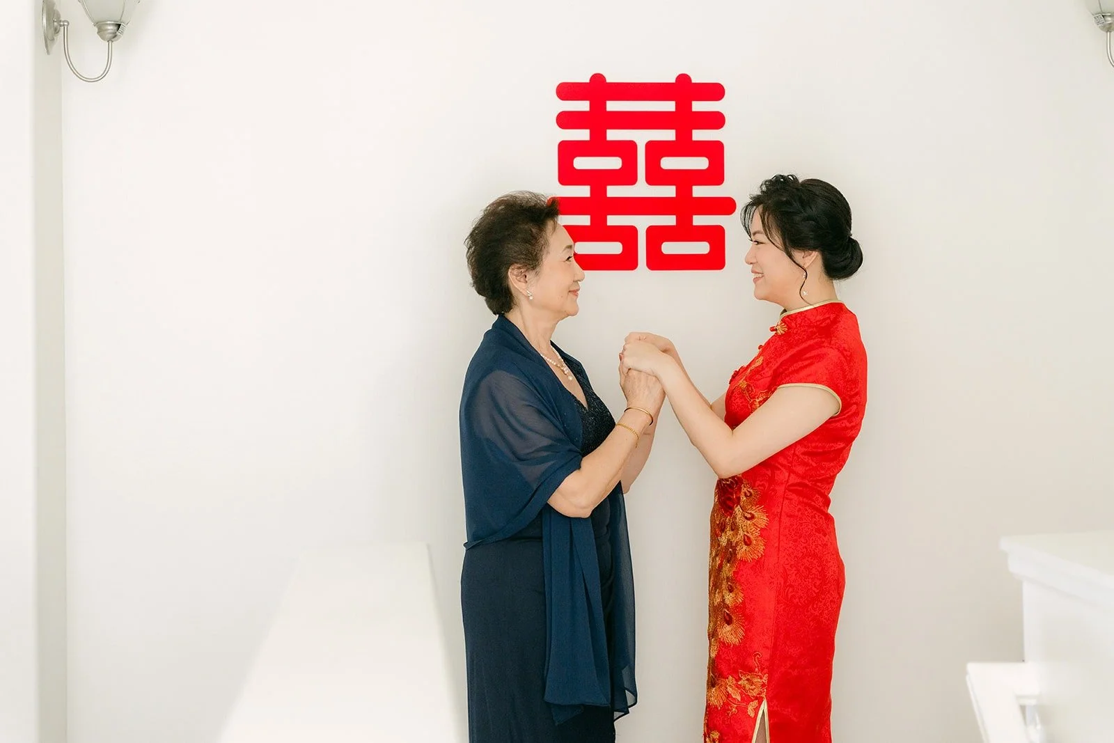Eunice holding hands with a family member in front of the double happiness sign