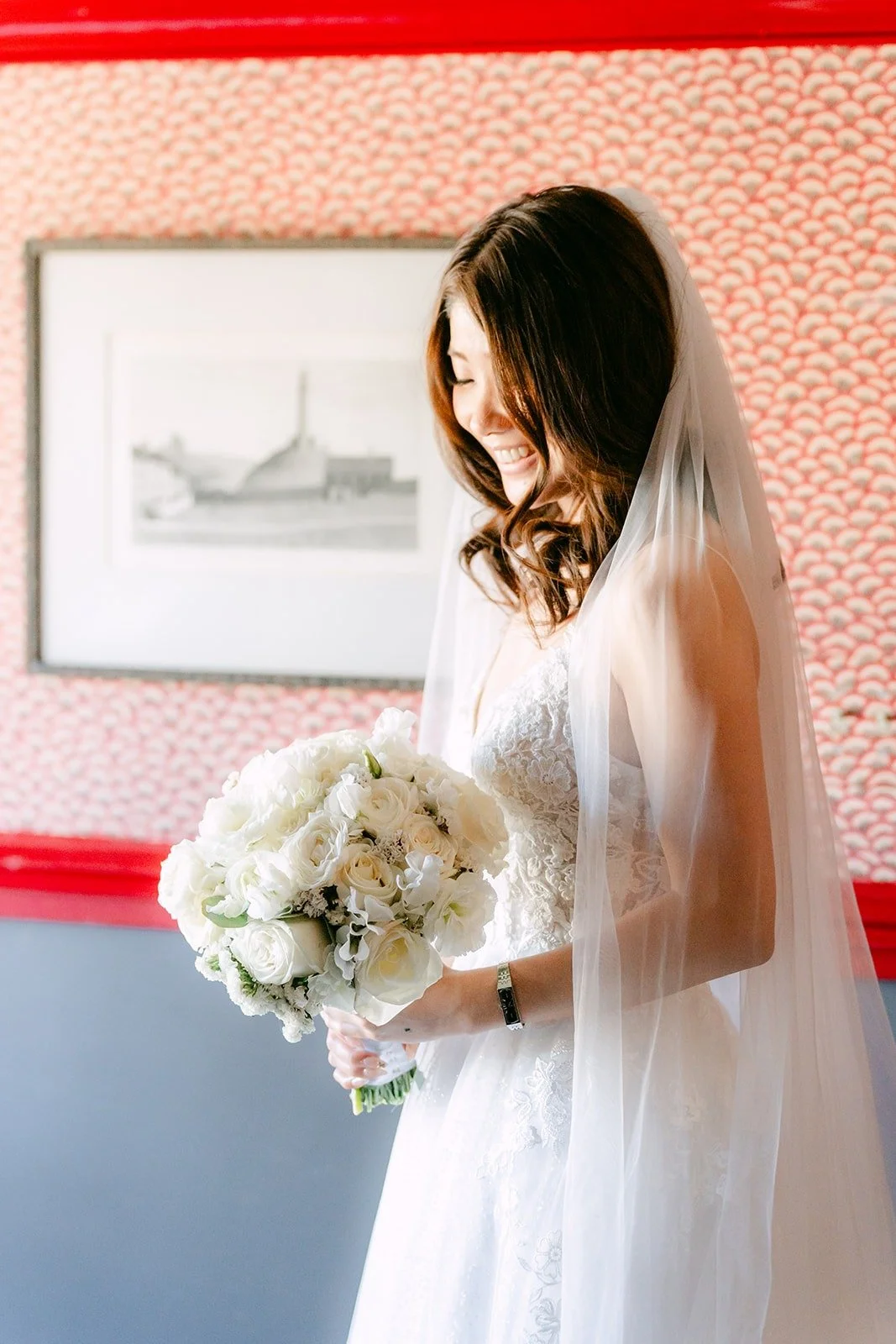 Valerie looking down at her bouquet in front of a red patterned wall