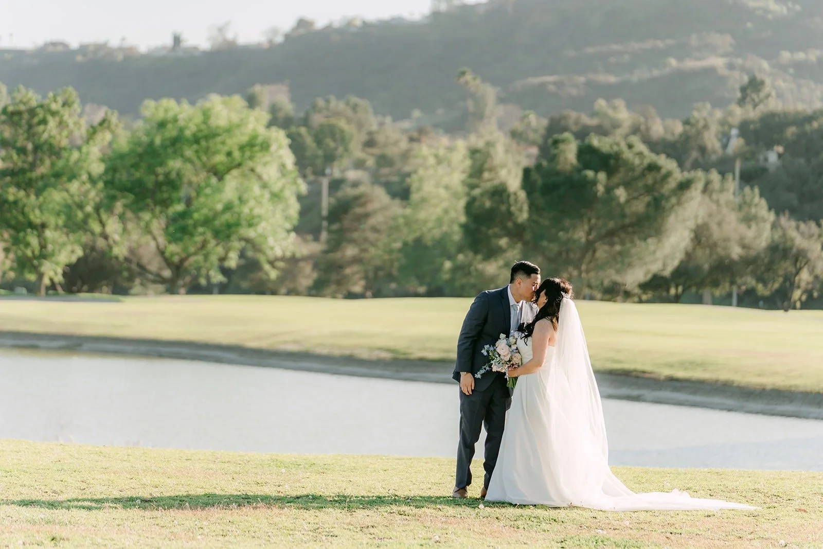 Florence and Jordan kissing by the pond with green hills behind them