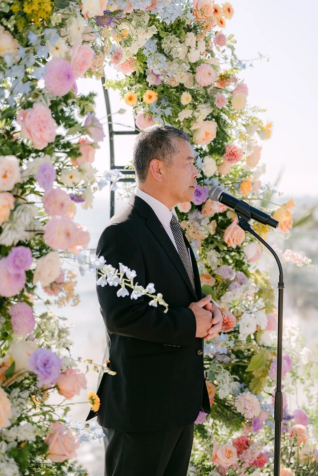 The officiant speaking into the microphone under the floral arch
