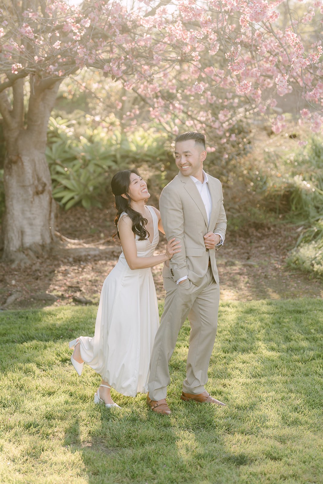 Kim and Vincent holding hands under a blossoming tree on the lawn.