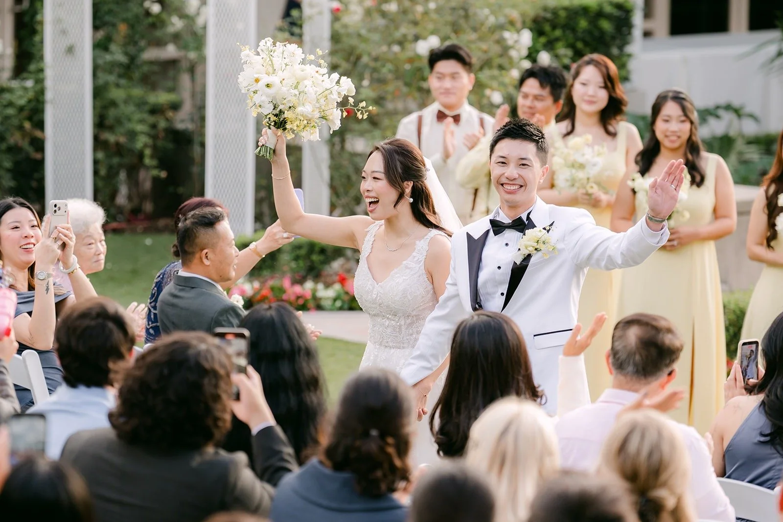 Jenny raising her bouquet and Ryan cheering as they head back up the aisle.