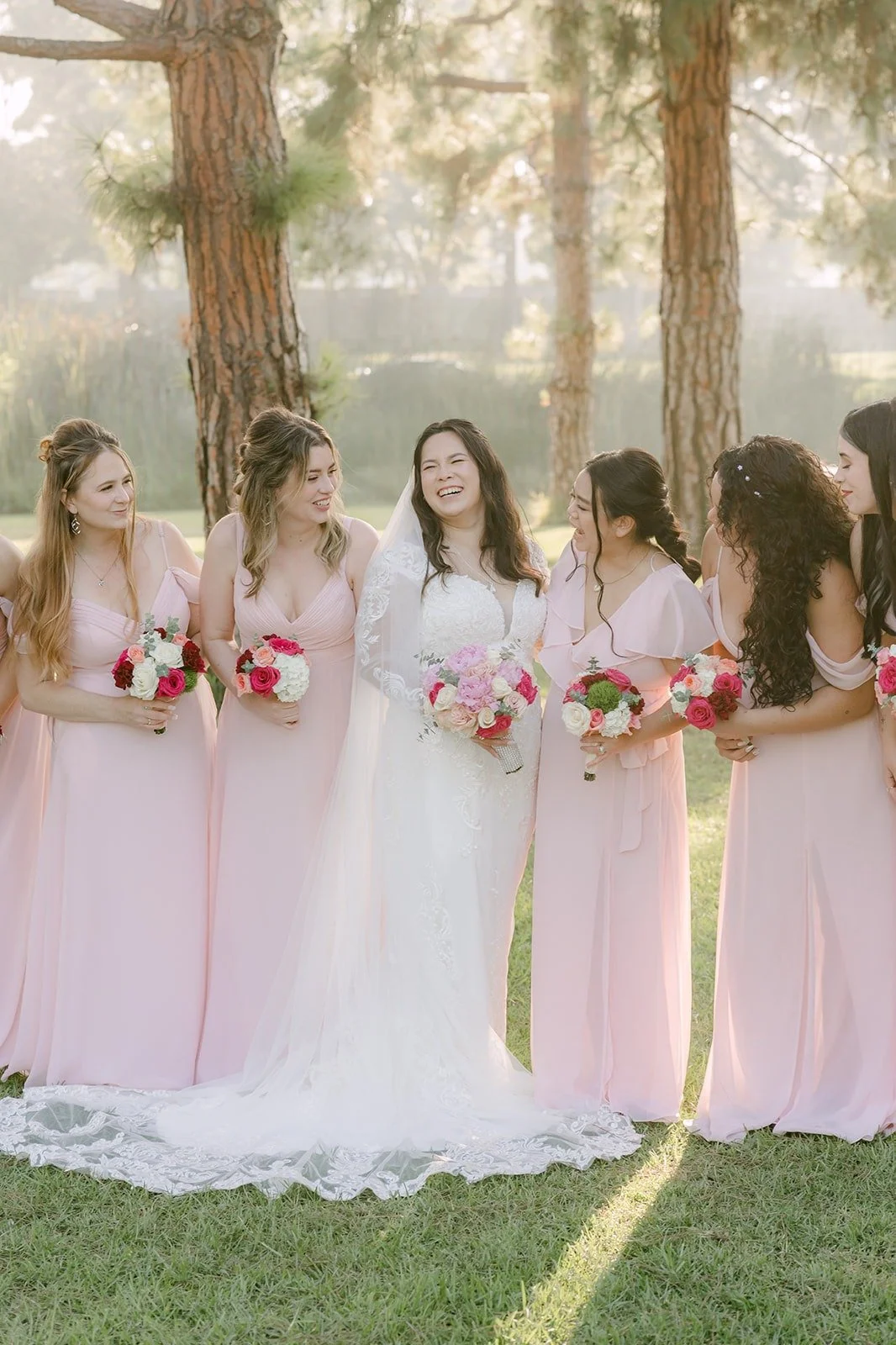 Amy with her bridesmaids in blush pink gowns under the trees