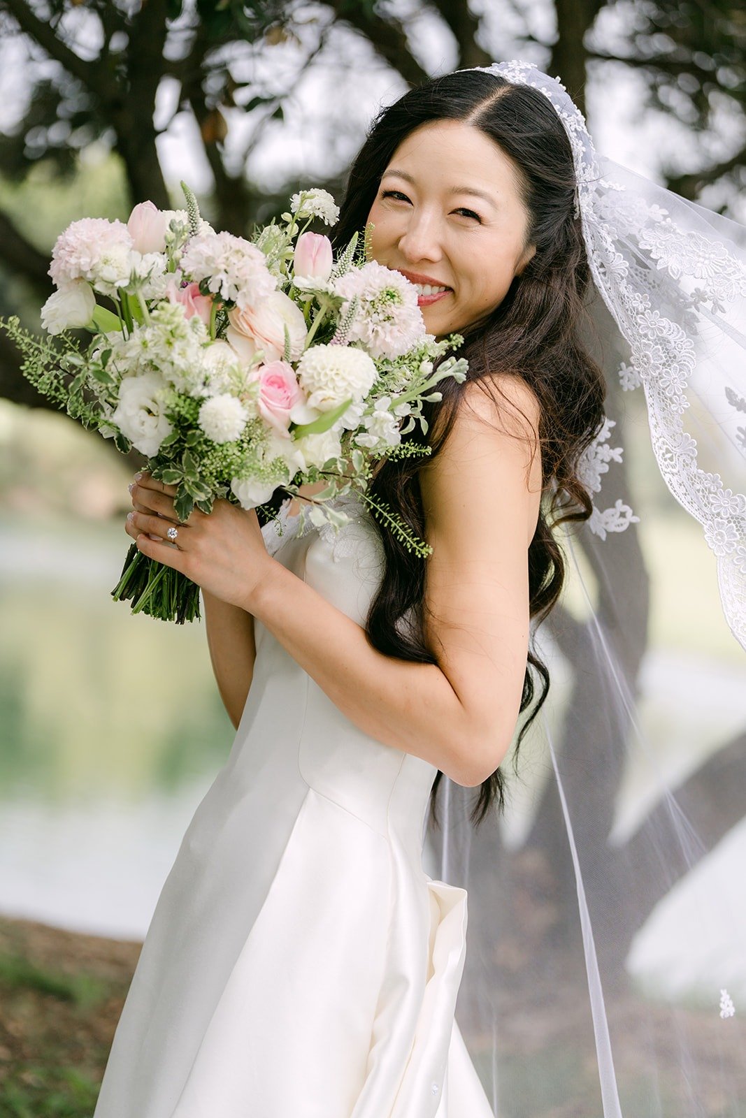 Kristine smiling with her bouquet under the trees at Los Coyotes Country Club