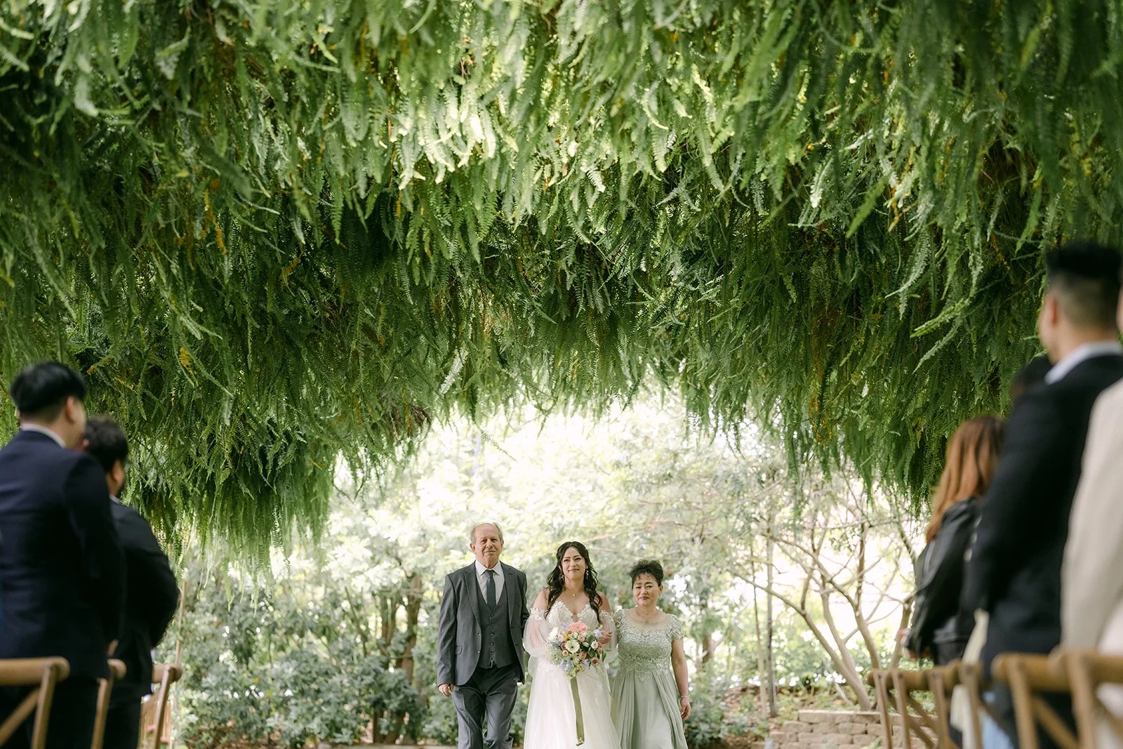 Kat walking down the fern covered aisle with her parents