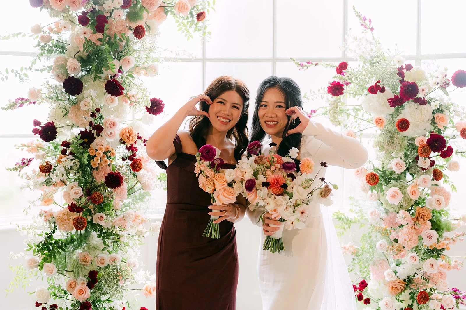 Denise and her sister laughing with their bouquets beside the florals.
