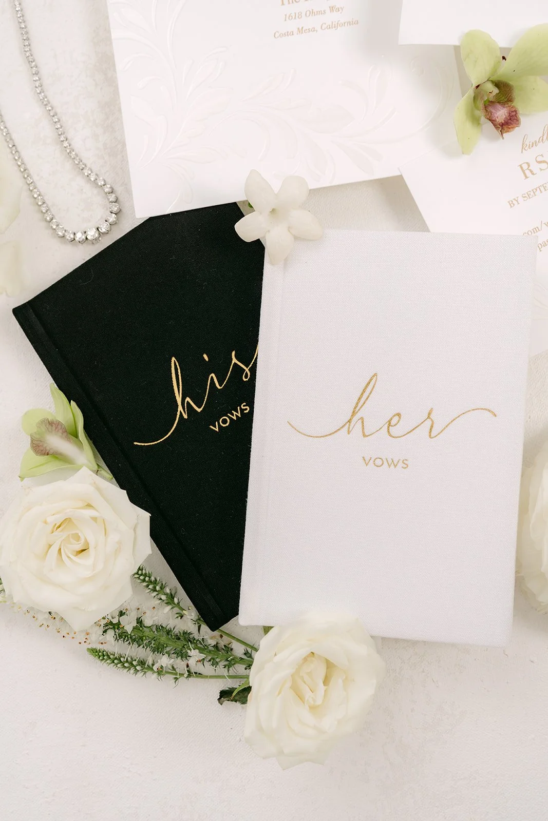 His and hers vow books with white roses and green orchids in the flat lay