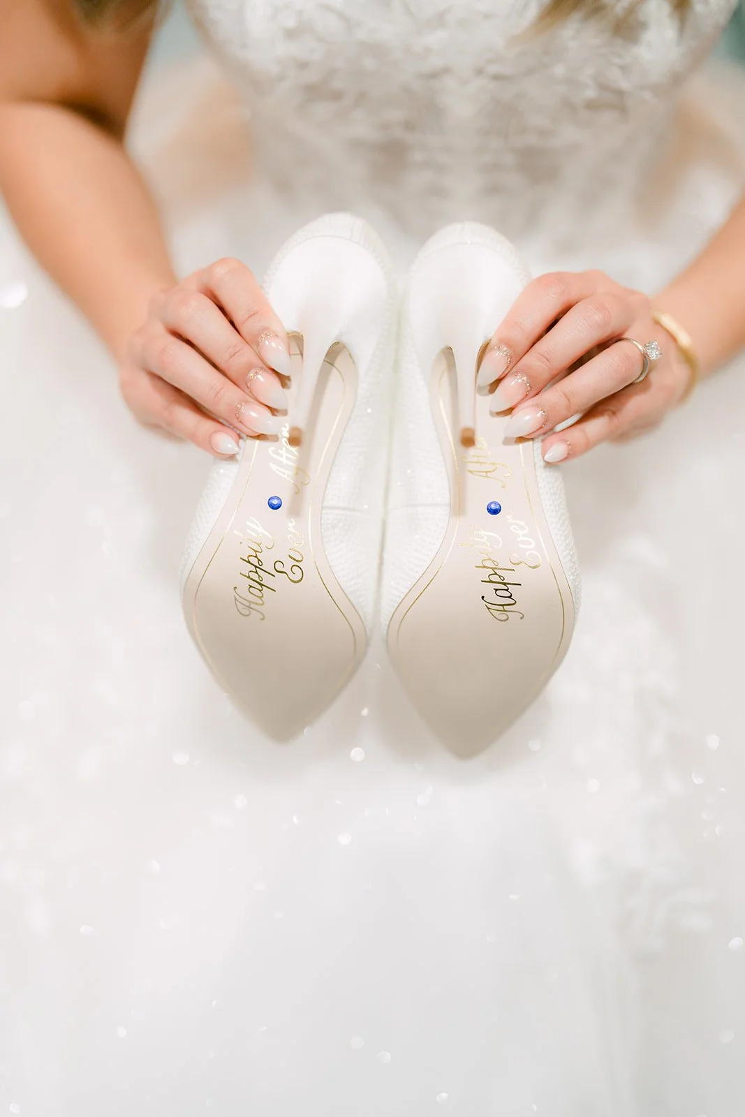 Bride holding her white wedding heels over her lace gown