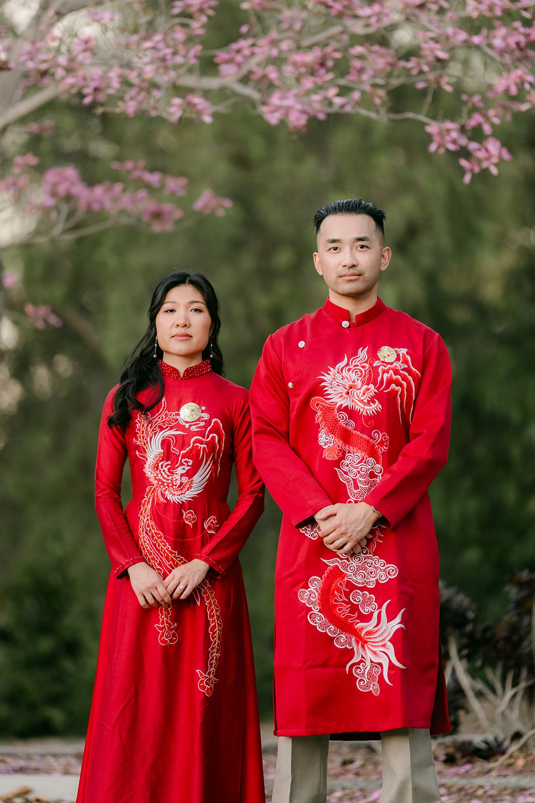 Kim and Vincent in red ao dai under a tree in pink bloom.