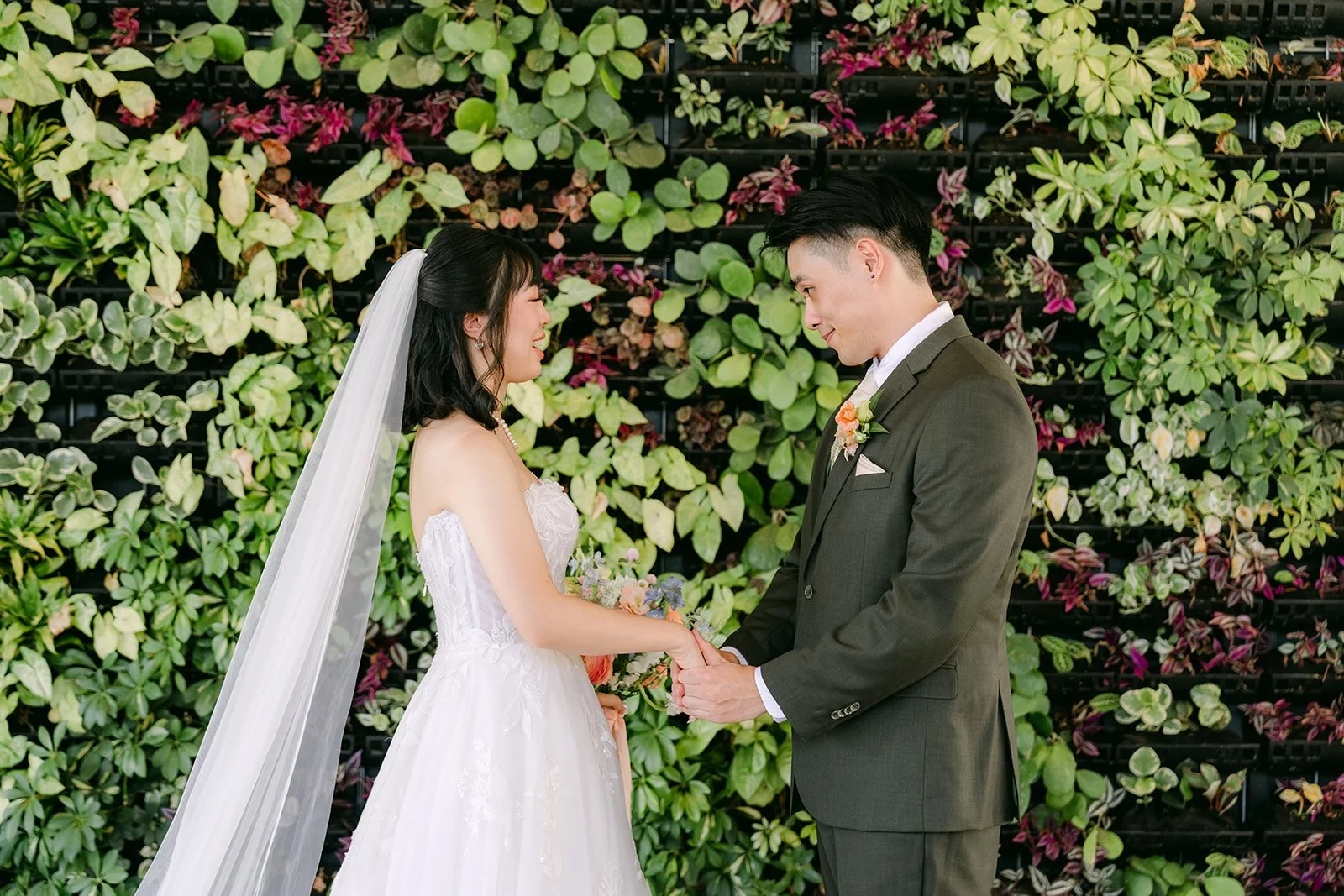 Vivian and Alex holding hands in front of the greenery