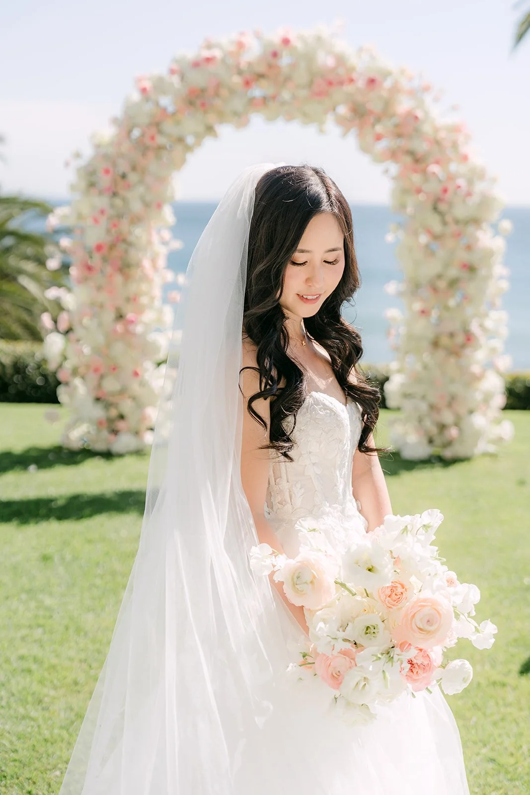 Bride in front of the blush floral arch holding her bouquet