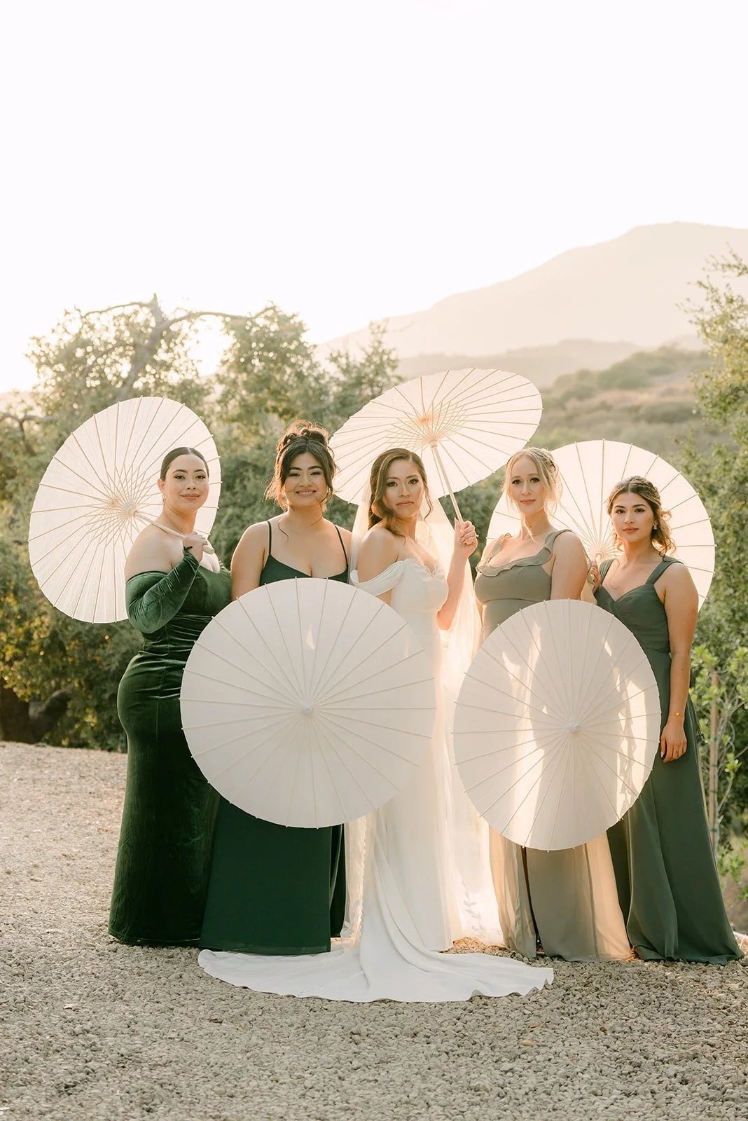 Mariana and her bridesmaids holding white parasols on the hillside