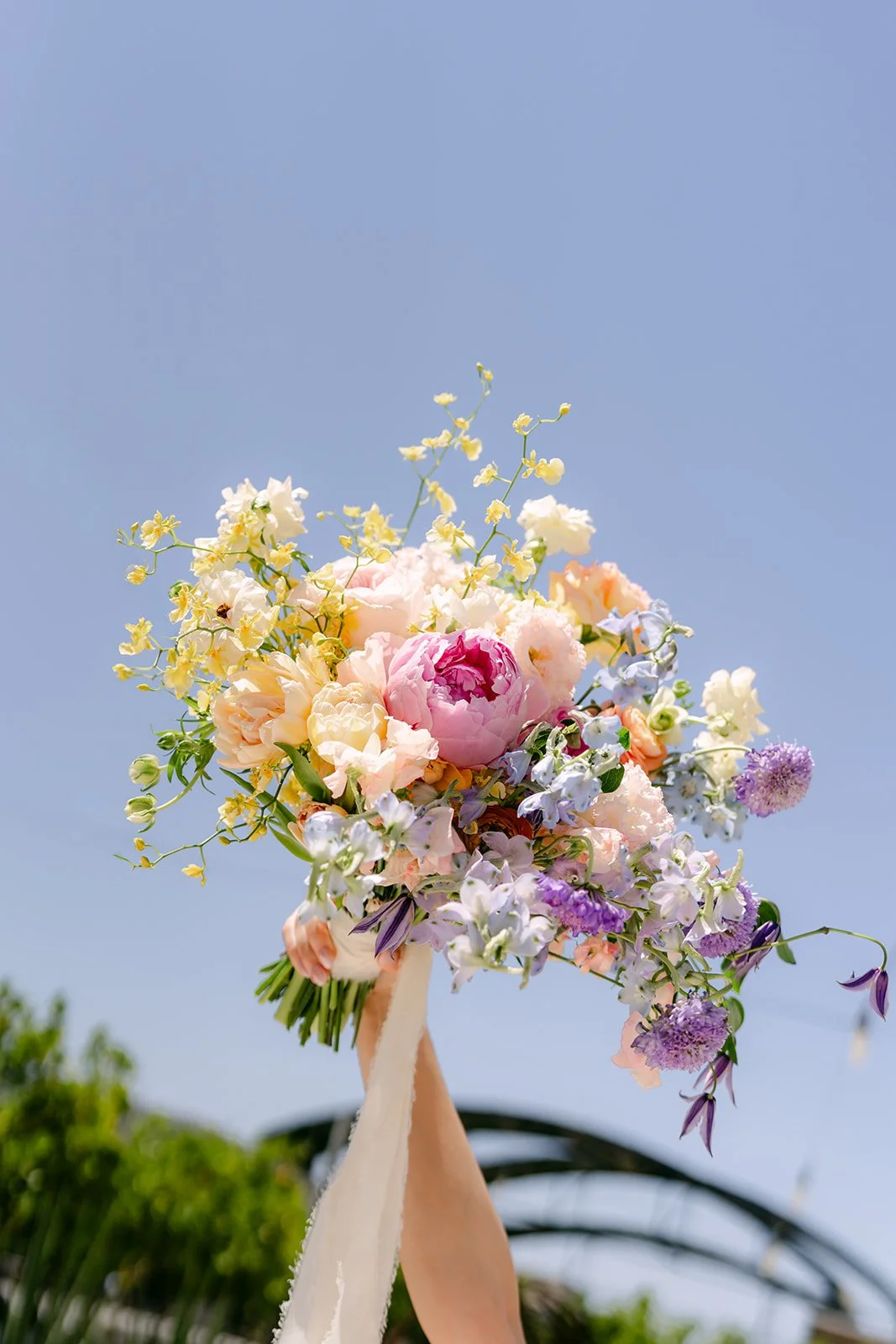 Pastel rainbow bouquet with ribbon held up against a blue Anaheim sky