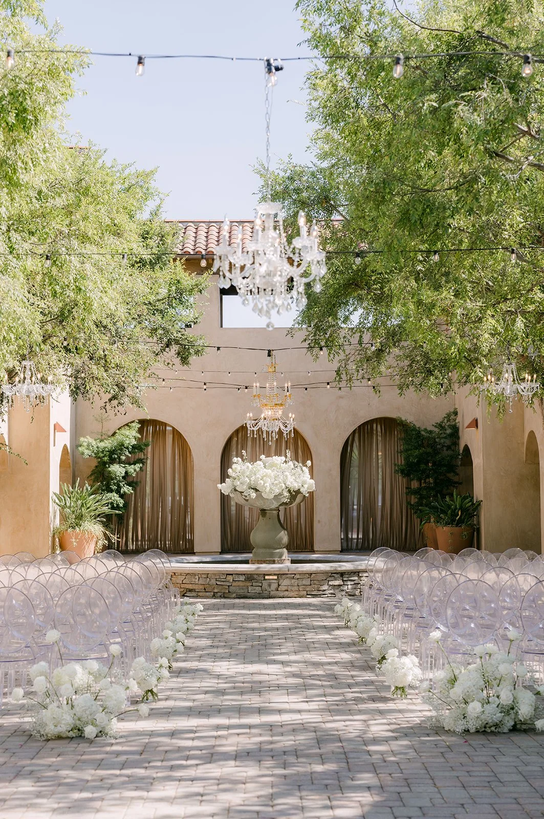 Serra Plaza courtyard ceremony aisle lined with white flowers and ghost chairs