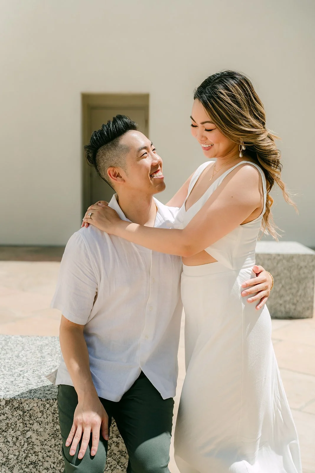 Stephanie leans into Alan as he sits on the granite block, both laughing.