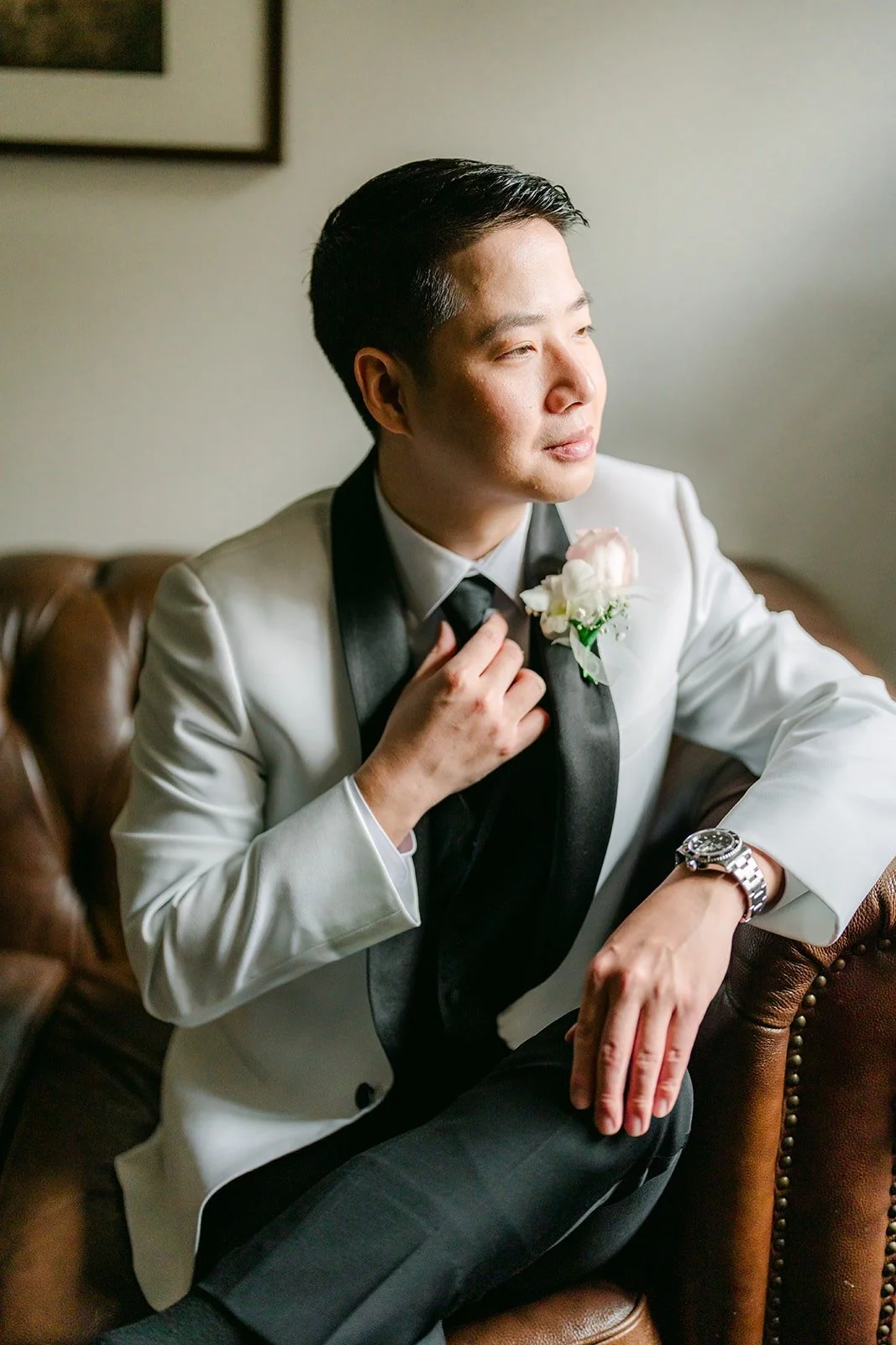 Chungman adjusting his tie in a white tuxedo jacket