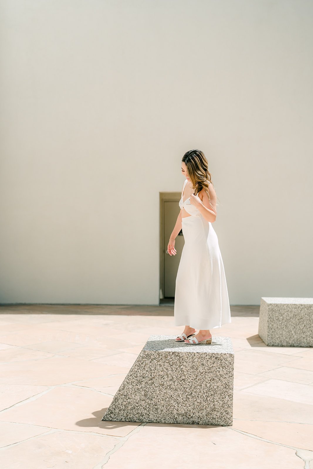 Stephanie standing on a granite block in front of the white walls of Noguchi Garden.