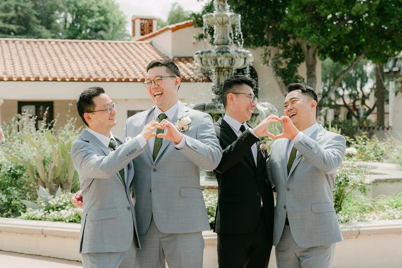 Eric and his groomsmen in gray suits make finger hearts at the fountain