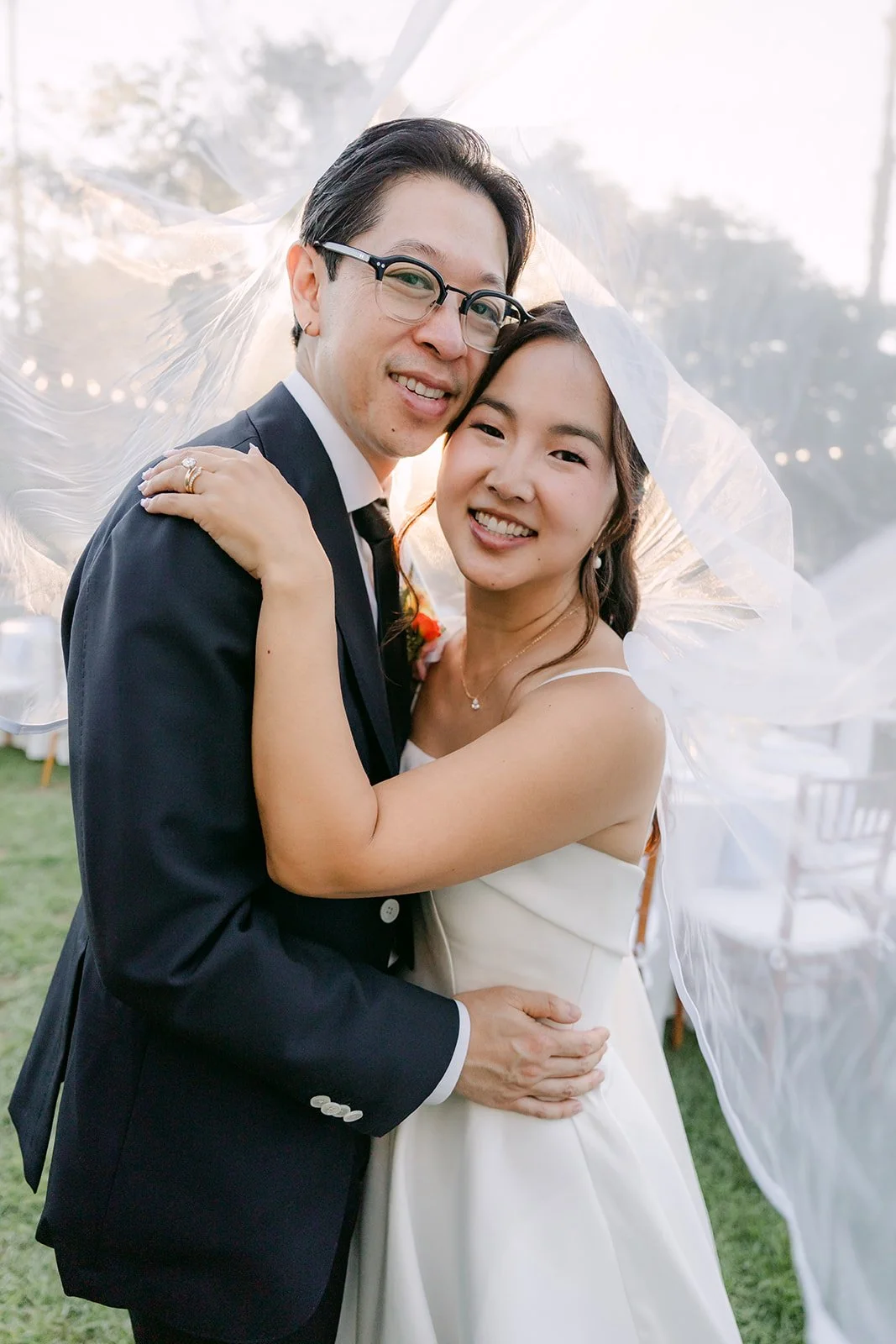 The newlyweds wrapped in the veil among the string lights