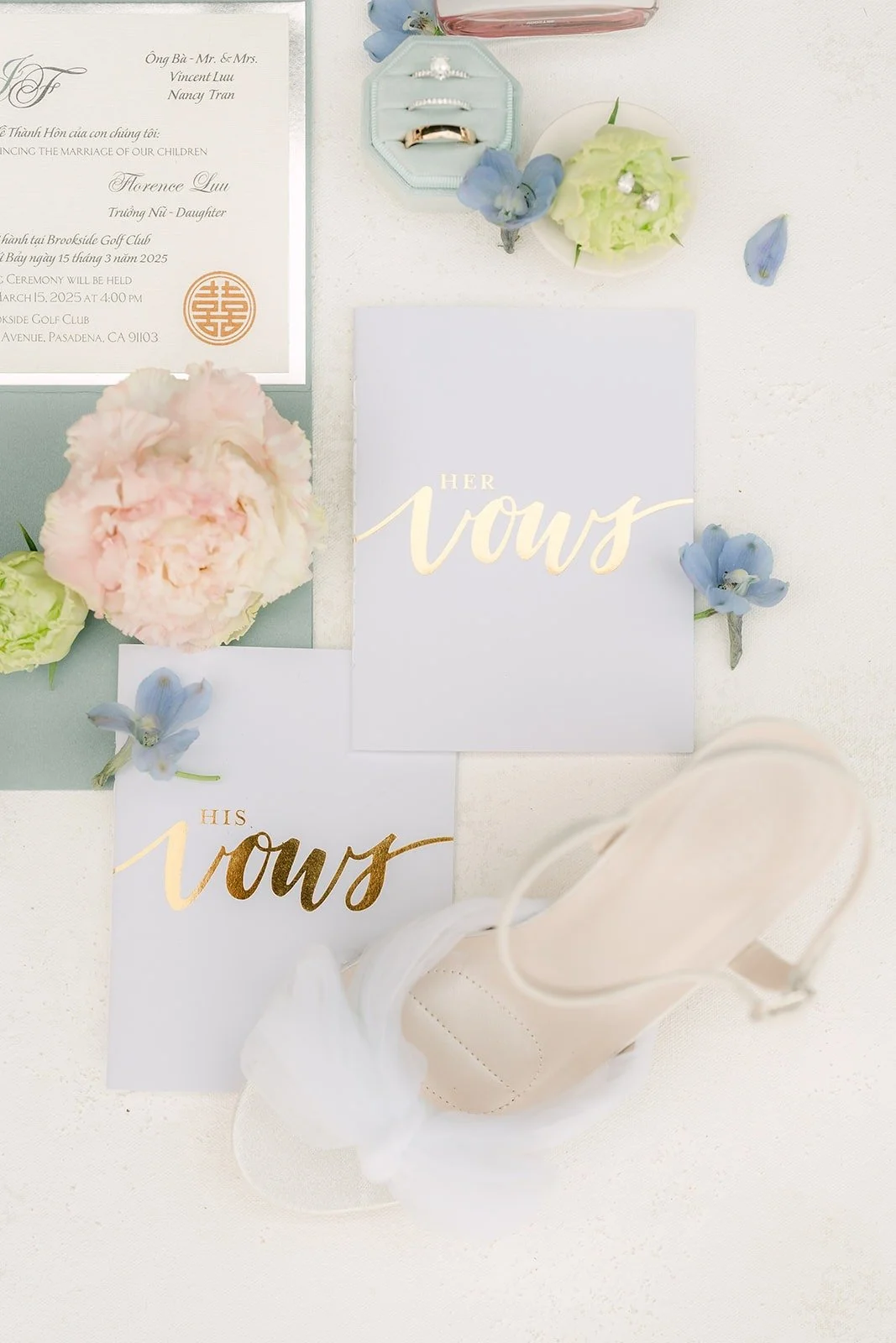 Vow books, invitation and bridal shoes styled with pale blue flowers