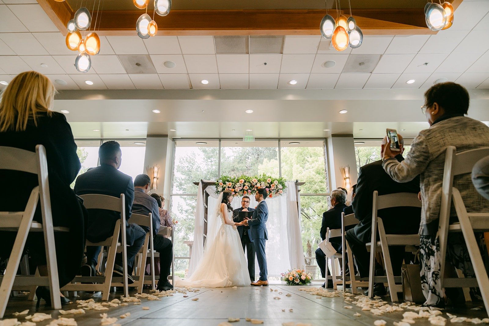 A wide view of the ceremony with guests watching Natalie and Mark under the floral arch