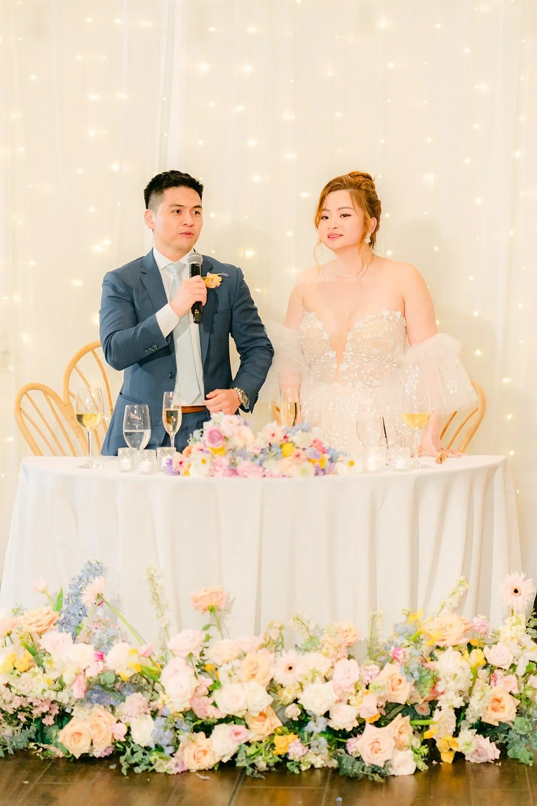 Joanna and Jerrick smiling at the sweetheart table during the speeches, photographed by One and Only Production