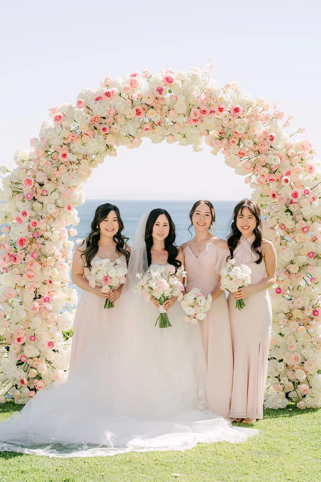 Bride with her bridesmaids holding bouquets under the floral arch