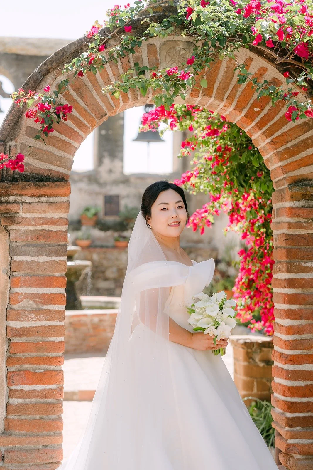 Chorok standing under a brick arch covered in pink bougainvillea at Mission San Juan Capistrano