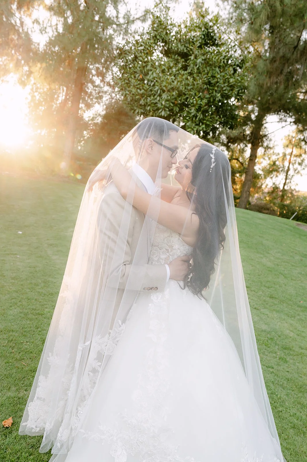 Sandra and Kevin kissing under her veil at sunset.