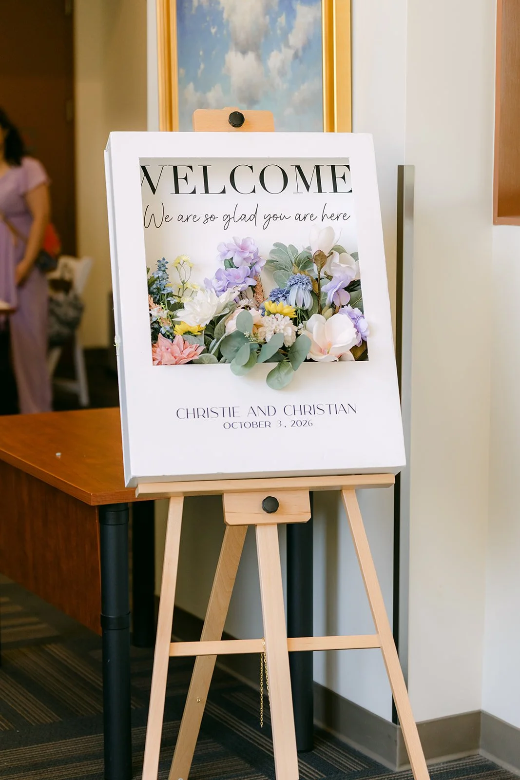 A welcome sign with the couple's photo and pastel florals at the entrance.