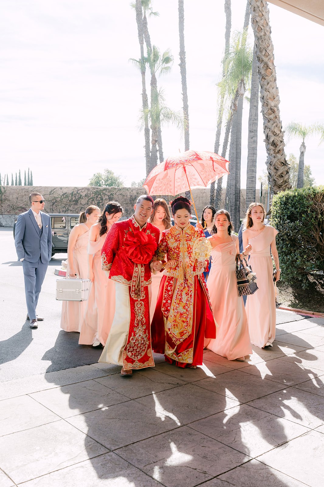 The wedding party walking down the driveway under a red umbrella, photographed by One and Only Production.