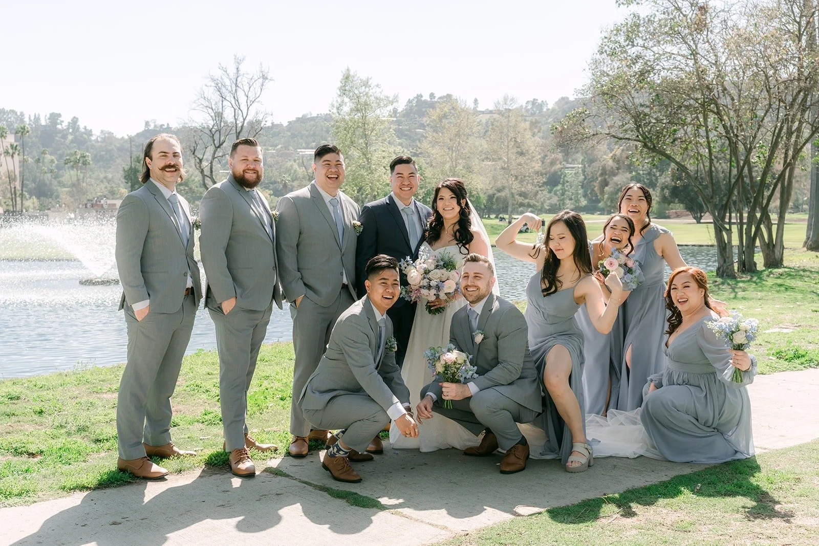 The wedding party in dusty blue and gray posed on the lawn