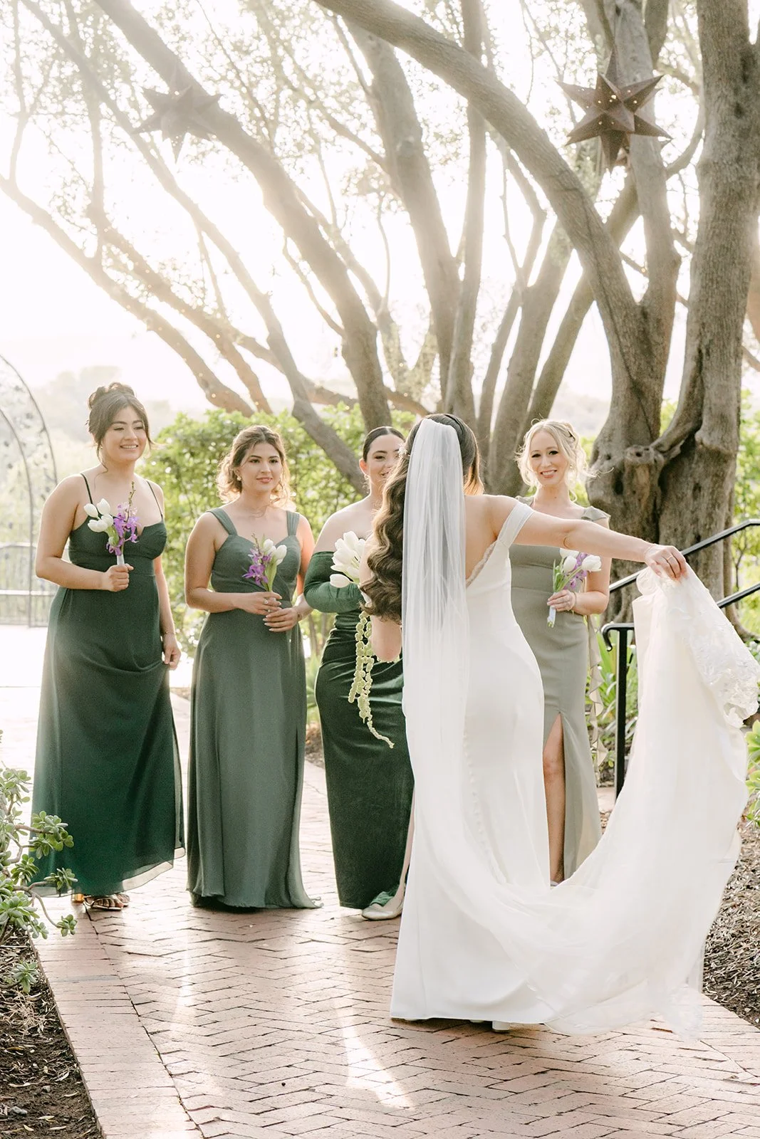 Bridesmaids arranging Mariana's train on the brick terrace beneath an olive tree