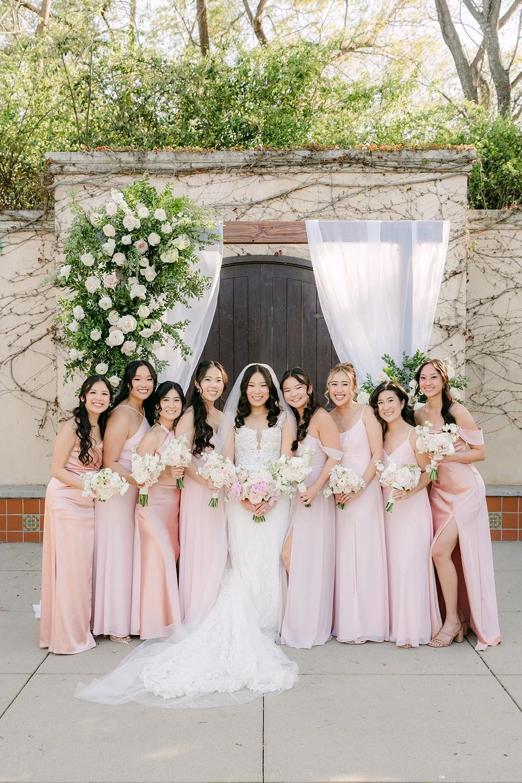 Kelli and her bridesmaids in blush in front of the floral arch at Los Robles Greens