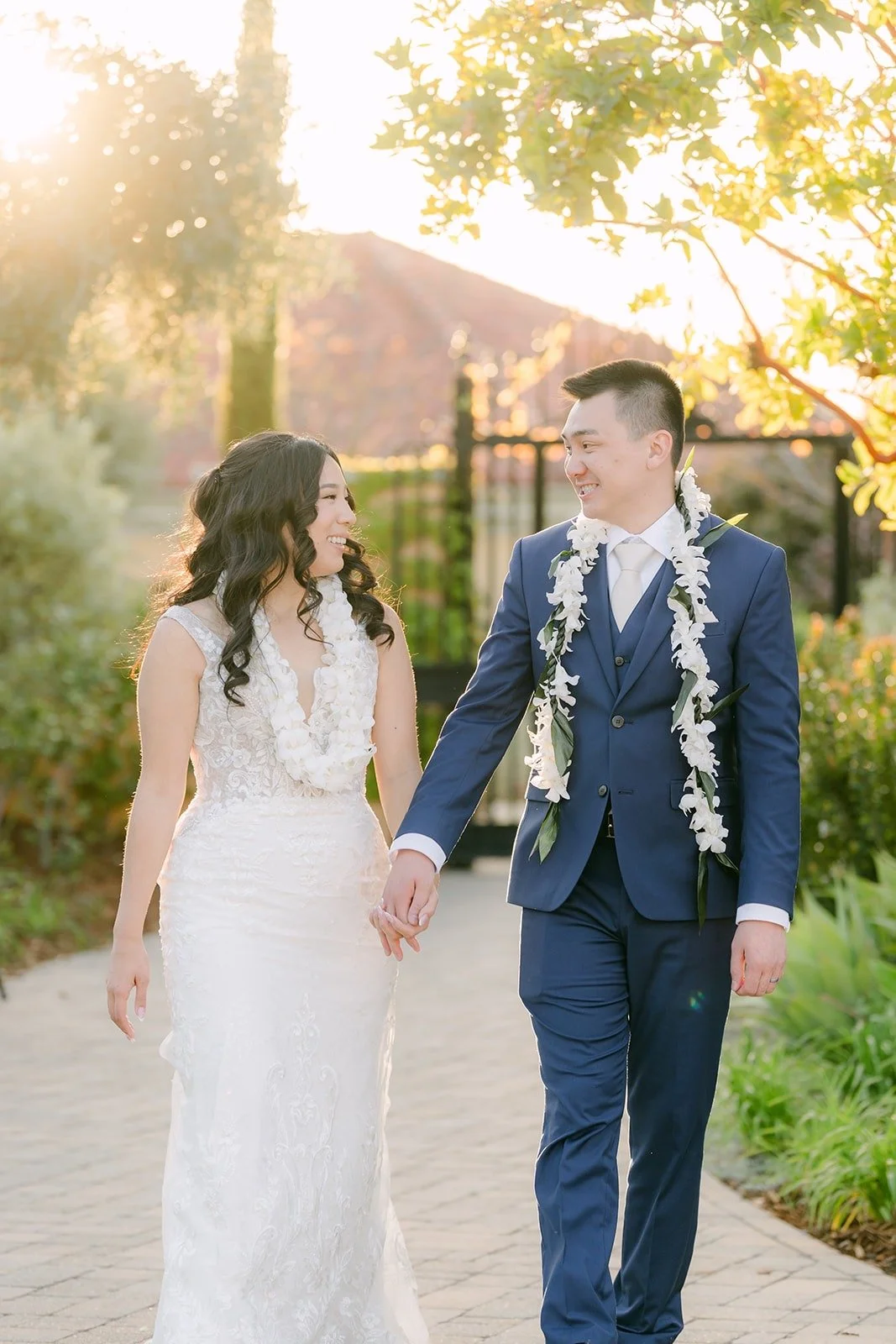 Kelli and Alex walking hand in hand in their leis at sunset